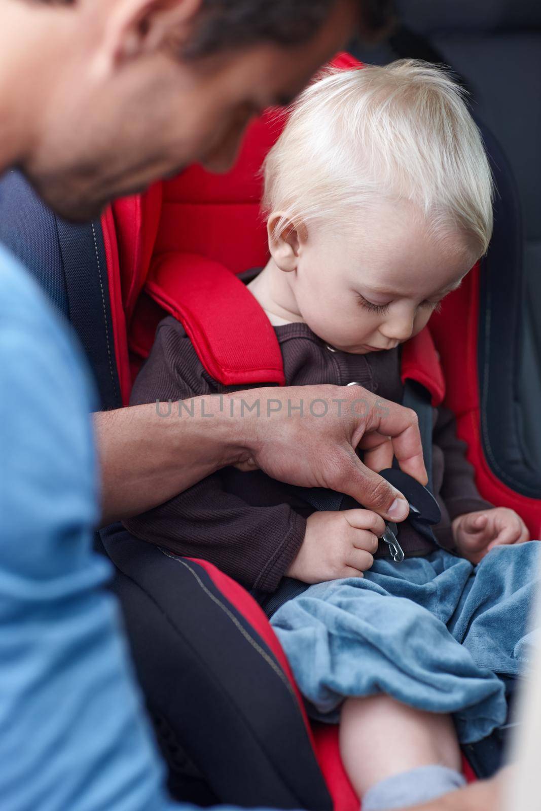 A father helping his child in a baby seat for the car.