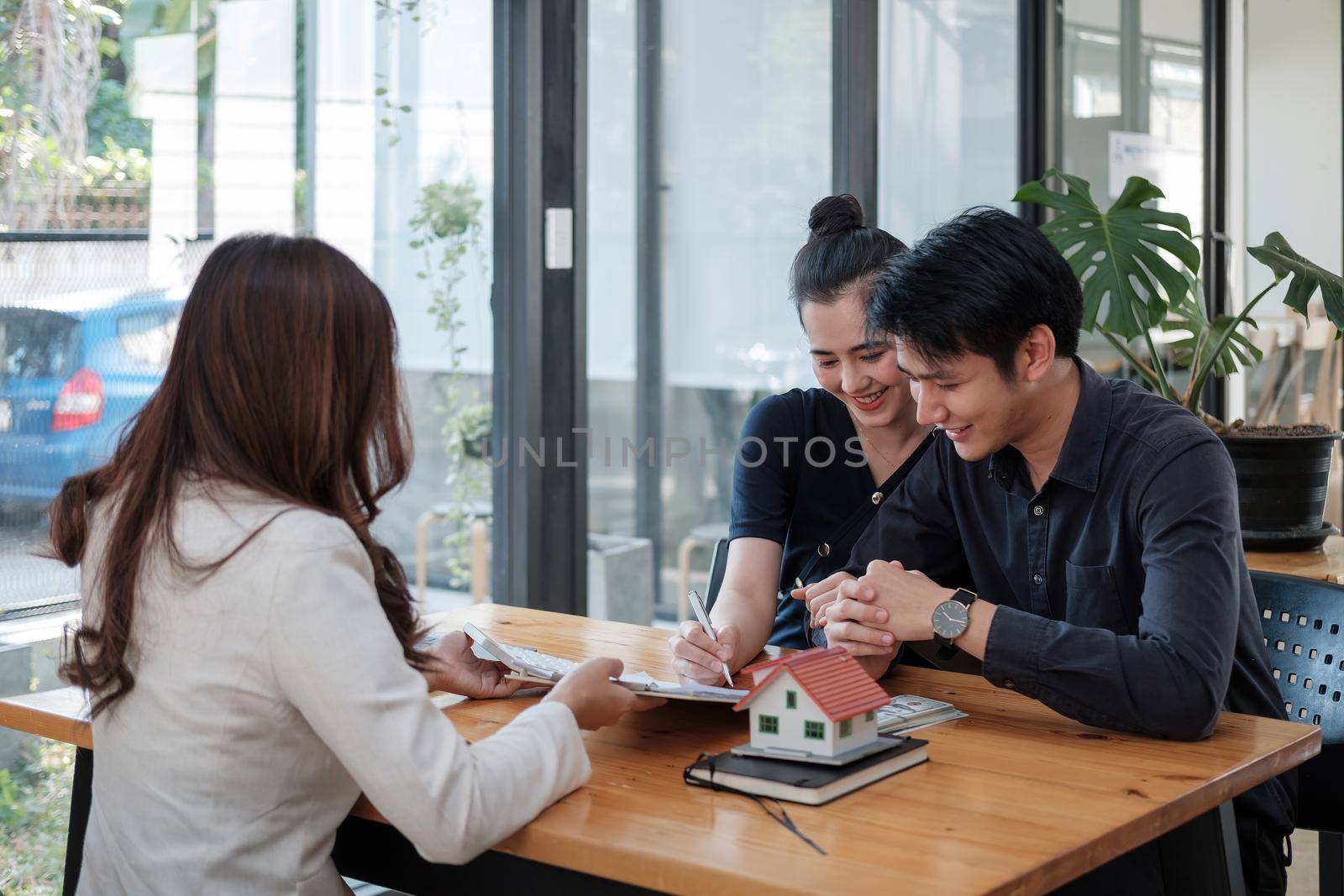 Real estate agent offer hand for customer sign agreement contract signature for buy or sell house. Happy asian couple signing a contract together at office. Real estate agreement concept.