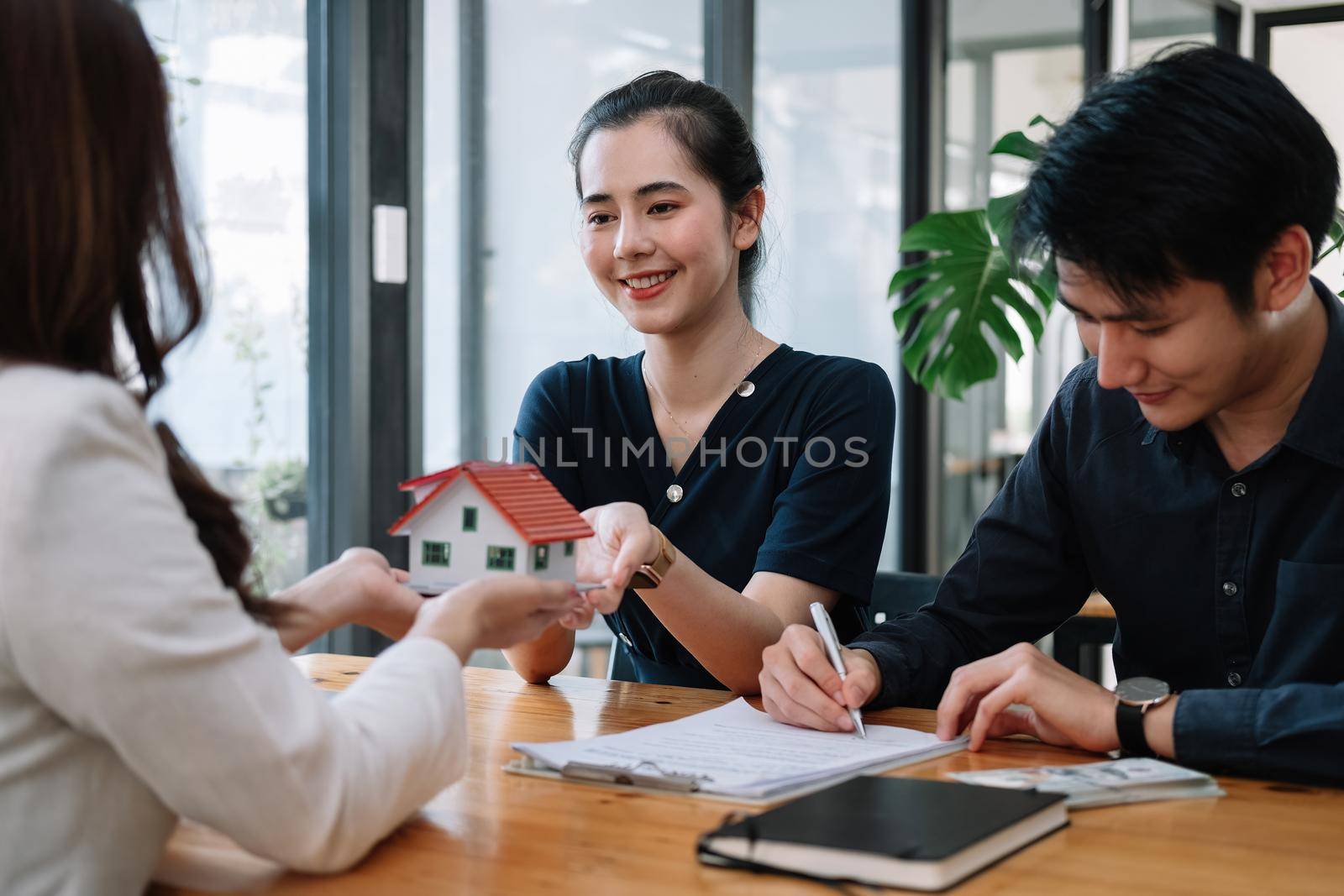 Real estate agent offer hand for customer sign agreement contract signature for buy or sell house. Happy asian couple signing a contract together at office. Real estate contact agreement concept.