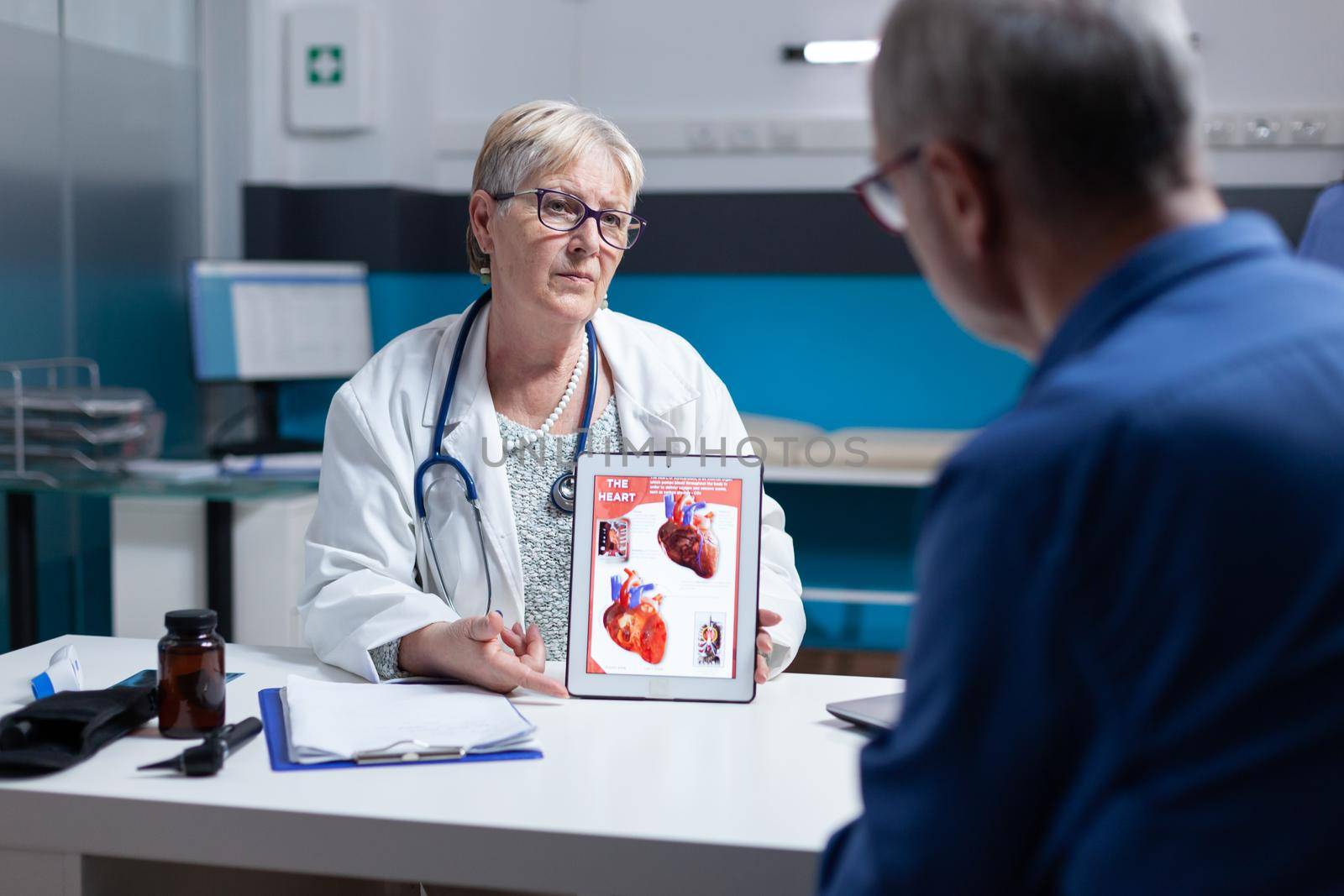 Physician explaining cardiology diagnosis with image of heart organ on tablet to patient. General practitioner showing illustration on cardiovascular system and anatomical structure to man.