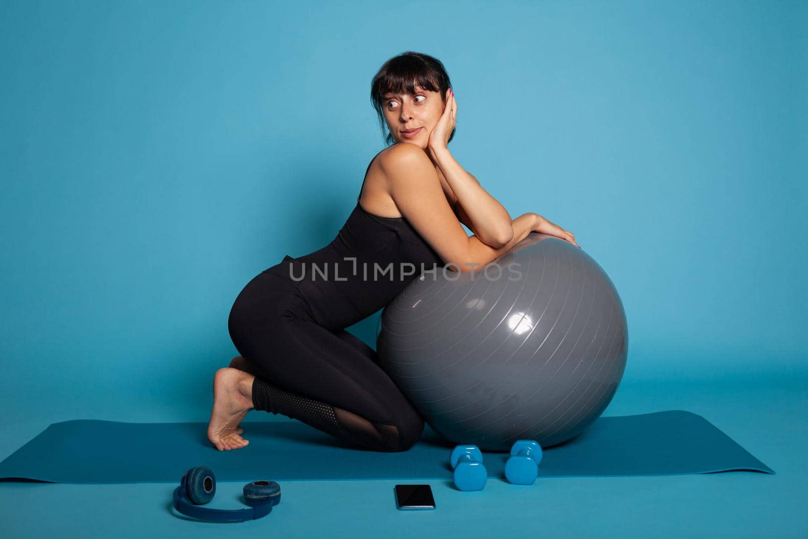 Happy trainer stretching body muscles using fitness fitball sitting on yoga ma by DCStudio