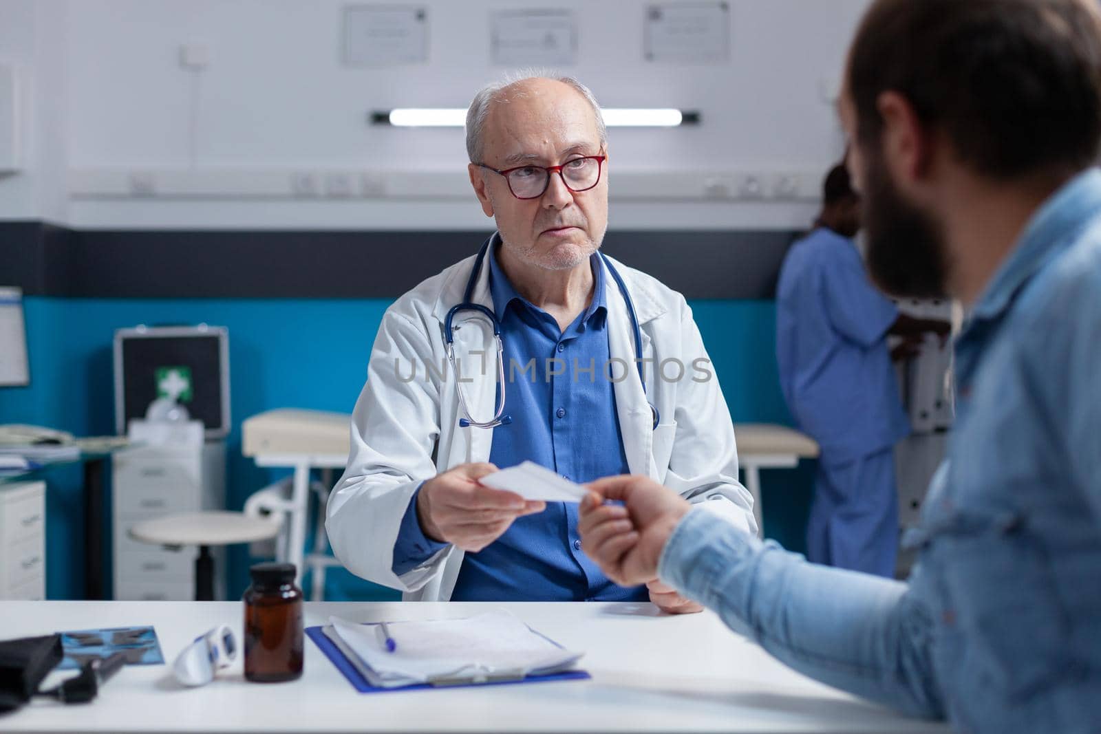 Physician giving prescription file to ill patient at checkup visit. General practitioner preparing treatment and medicine for man with disease, after medical examination in cabinet.