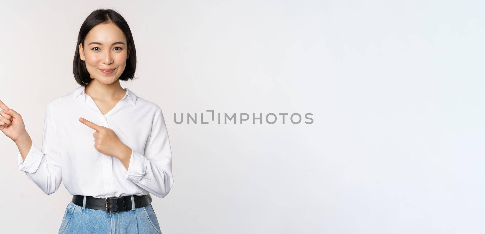 Image of smiling young office lady, asian business entrepreneur pointing fingers left, showing client info, chart of banner aside on copy space, white background by Benzoix