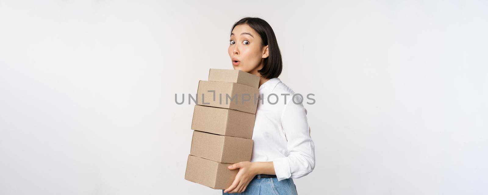 Portrait of young asian woman holding boxes, carry delivery goods. Korean female entrepreneur assemble order, standing voer white background by Benzoix