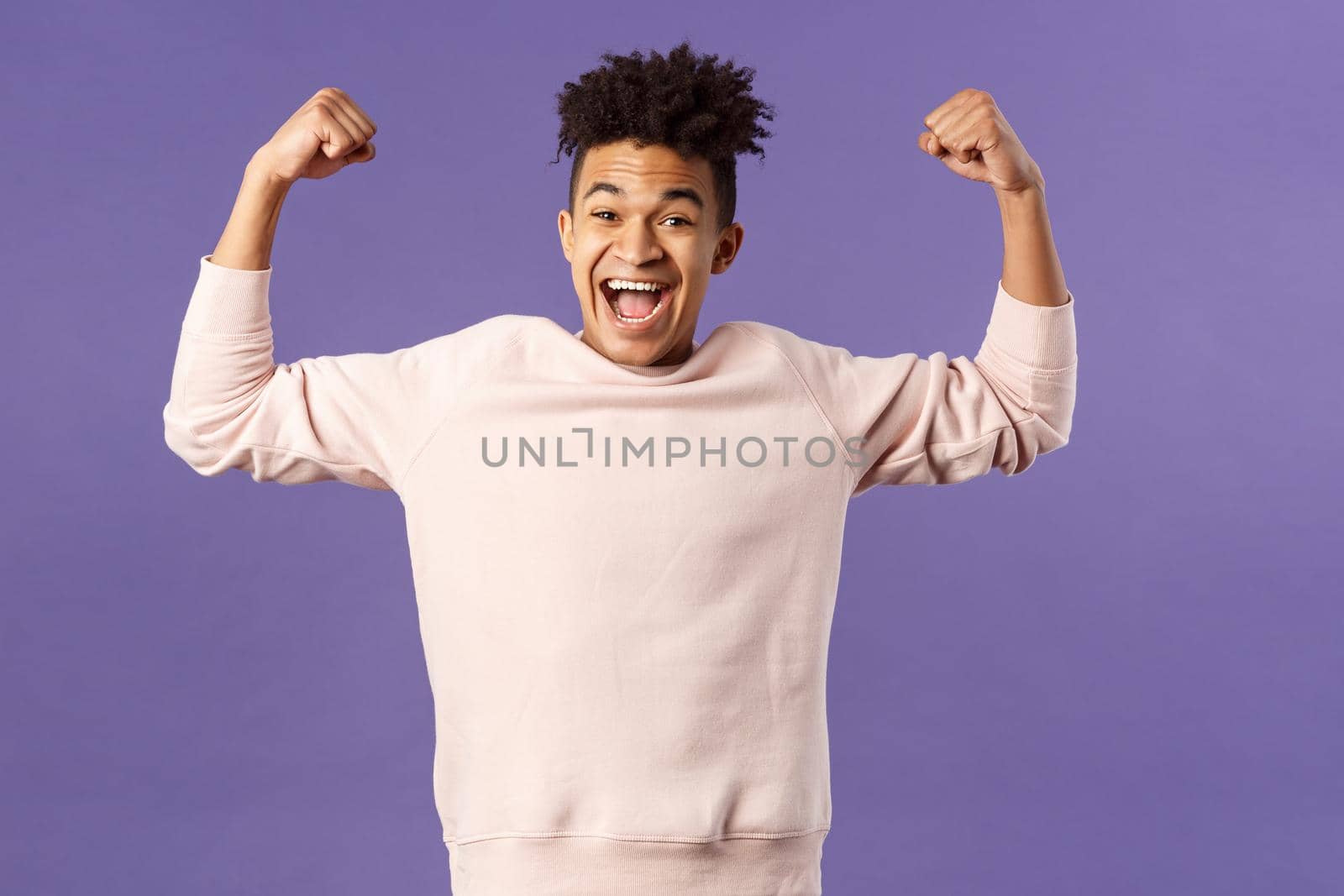 Portrait of young happy man got scholarship, applied to cool university, raise hands up flex biceps like champion, triumphing from great news, achieve goal and rejoicing, purple background by Benzoix