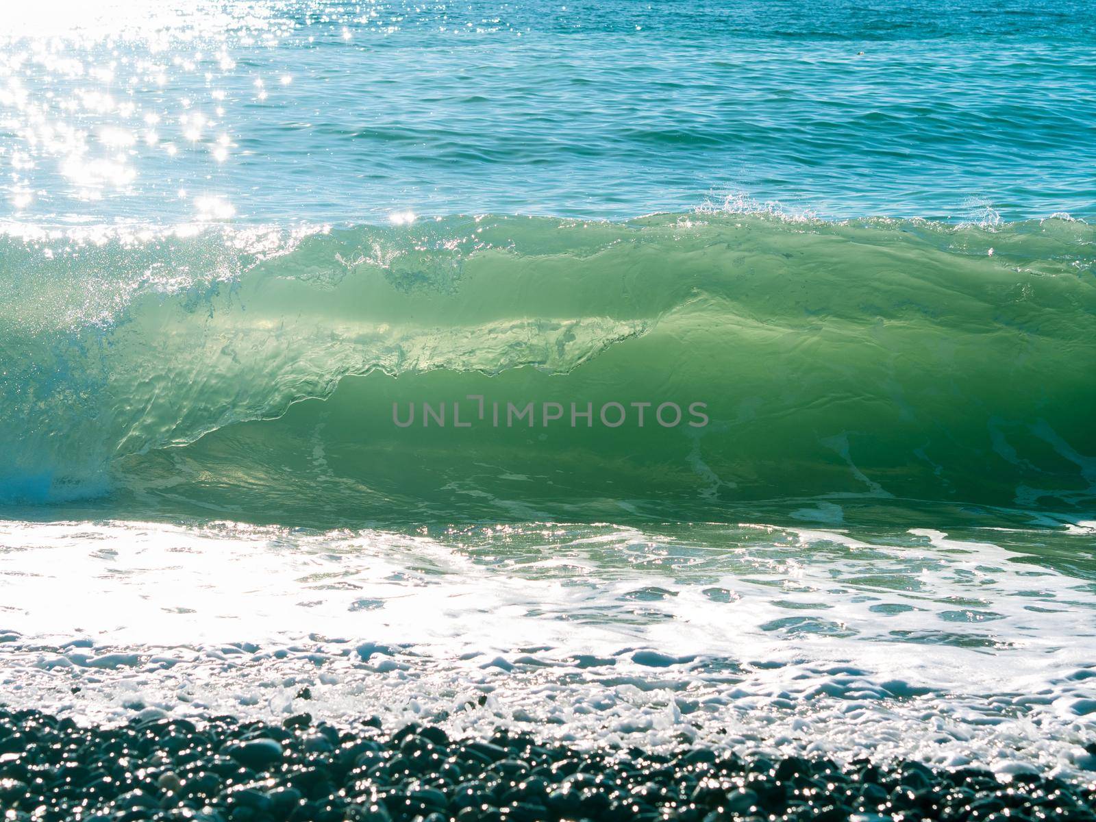 Sea wave with foam, beach, pebble, sun glare on the water, black sea coast. Horizontal framing.