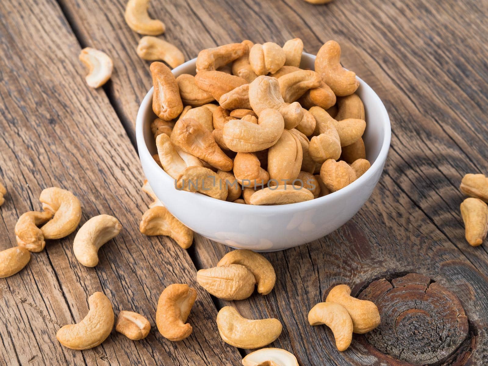 Cashew nuts in white cup on brown wooden background, side view