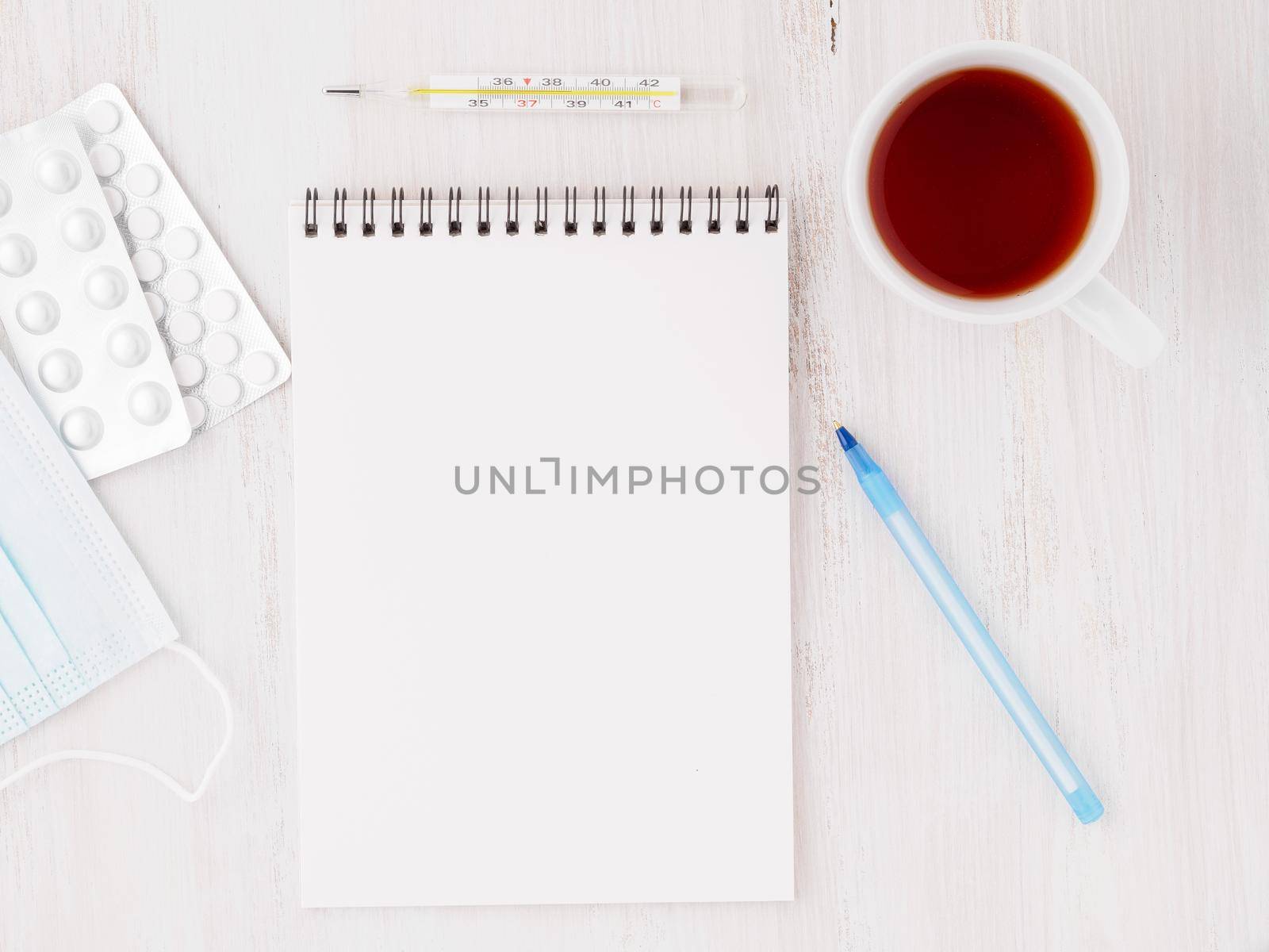 open notebook with blank white clean page to write the treatment plan of the illnedd. Pills, pen, paper, thermometer on white wood background, top view.