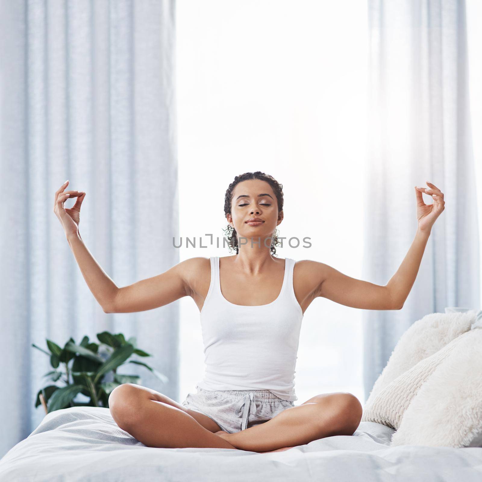 Start your day on a peaceful note. Shot of an attractive young woman meditating while sitting on her bed in the morning. by YuriArcurs