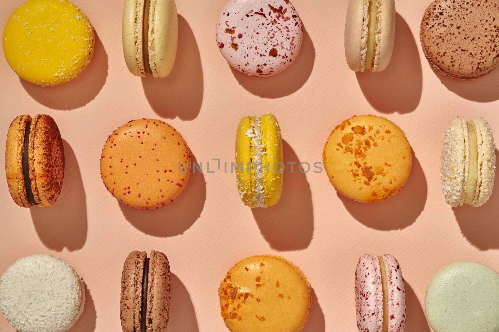 Top view of colorful sandwich-cookie macarons on pink background pattern