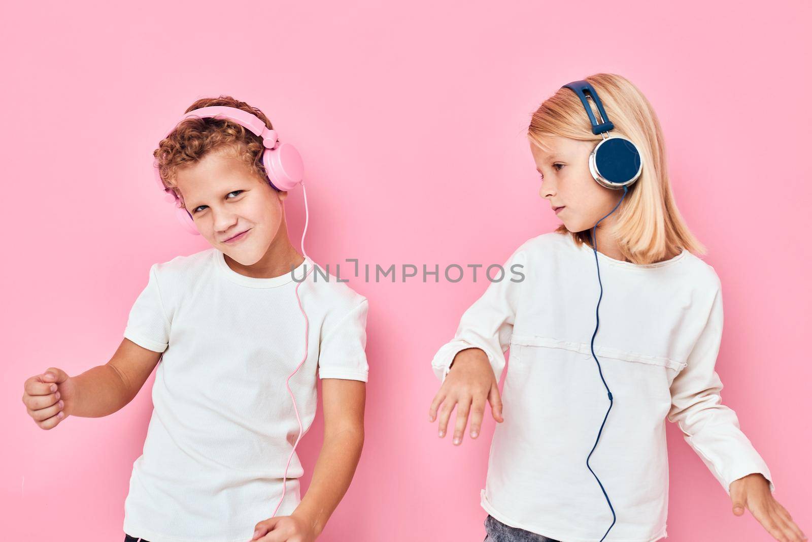 Funny children stand next to in headphones pink color background. High quality photo