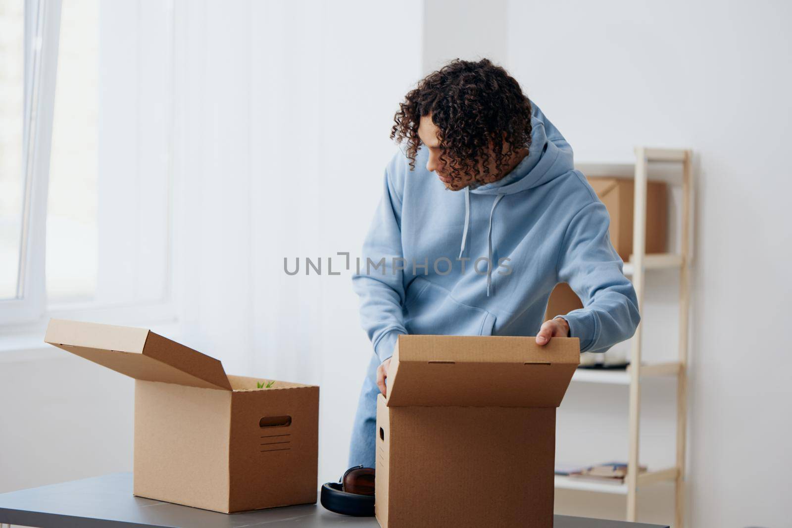 A young man in headphones unpacking with box in hand sorting things out by SHOTPRIME
