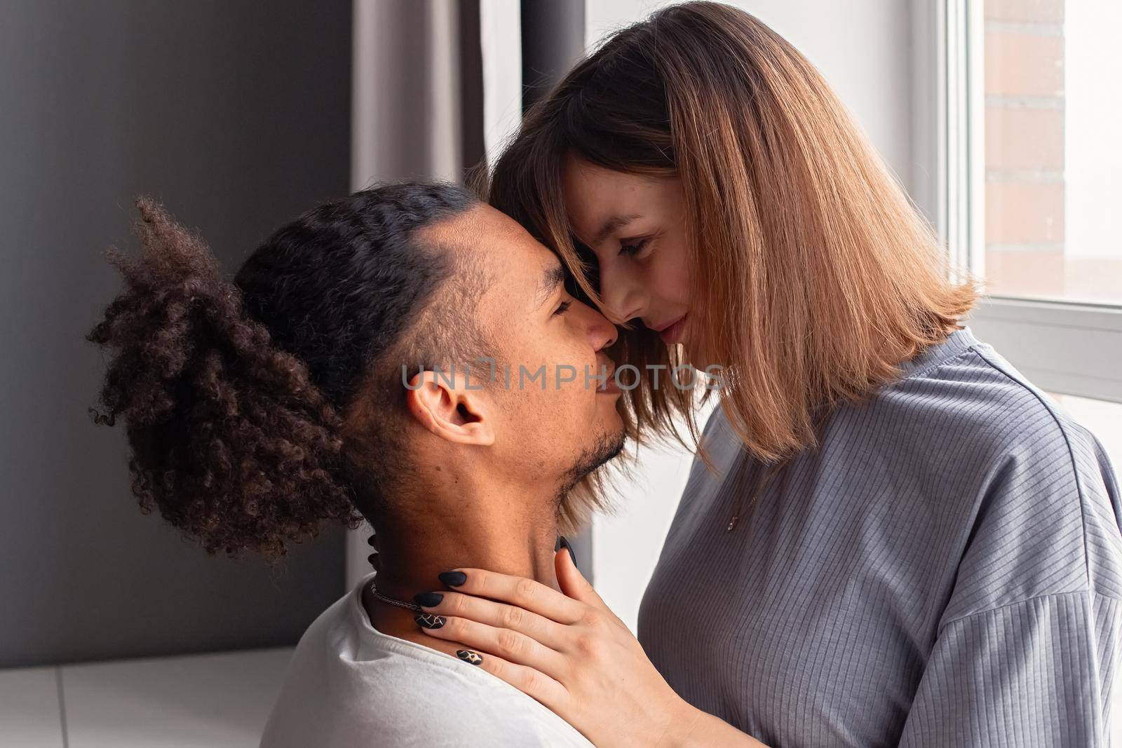 Portrait of multiracial couple, guy and girl face to face, sitting by the window