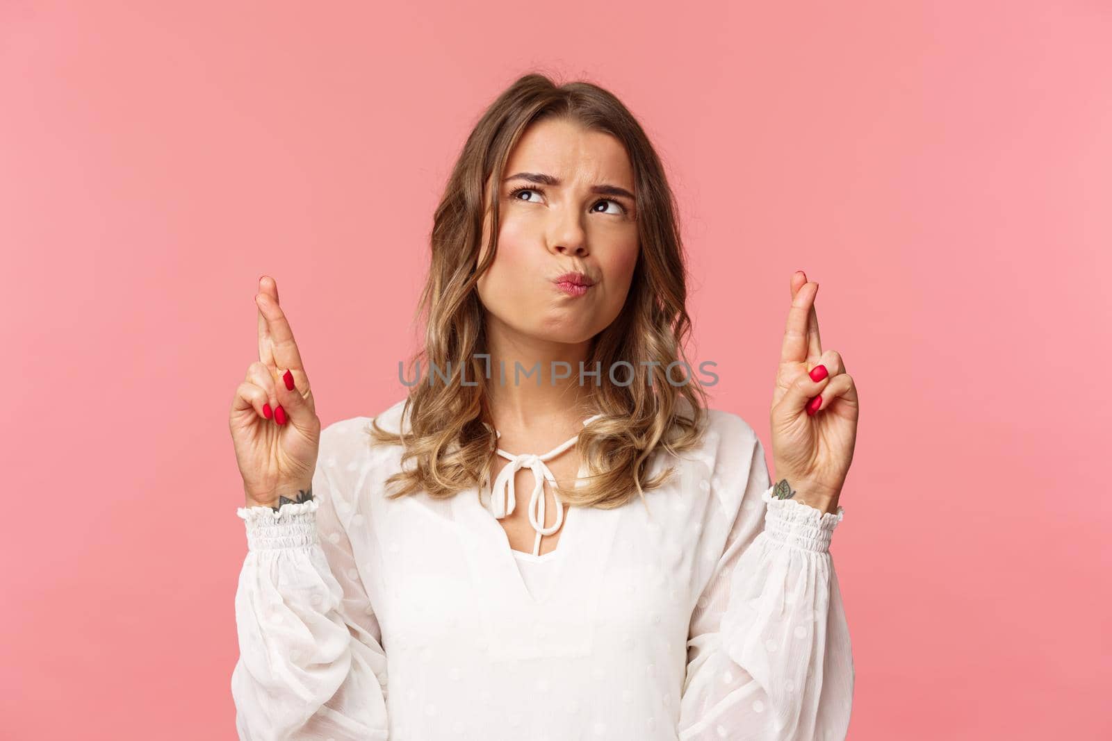 Close-up portrait of hesitant and thoughtful attractive blond girl making assumption, cross fingers good luck, squinting uncertain while thinking and looking up, standing pink background.