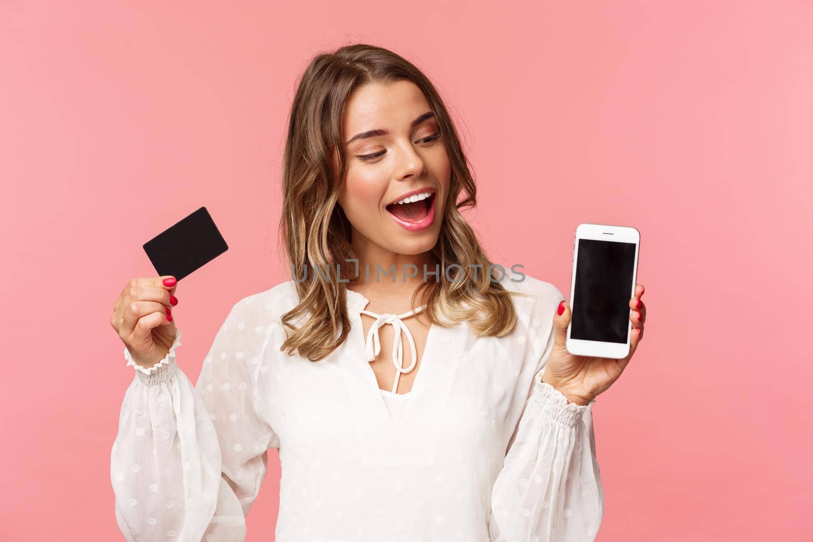 Finance, shopping and technology concept. Close-up portrait of excited good-looking blond girl in white dress, renew her spring wardrobe with buying clothes online via smartphone, hold credit card.