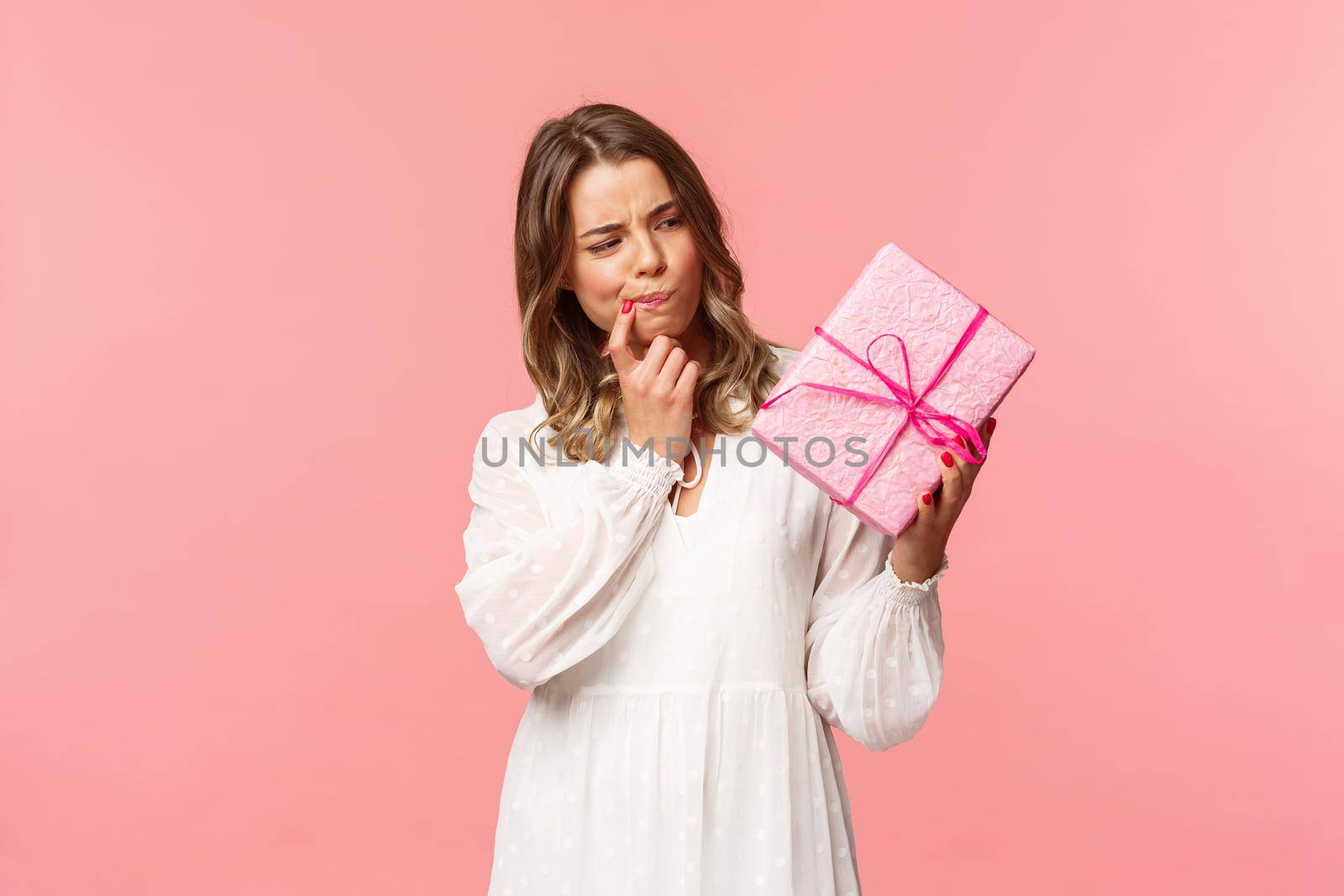 Holidays, celebration and women concept. Portrait of thoughtful curious blond girl thinking whats inside gift box, look pondering say hmm as making assumpion, standing pink background.