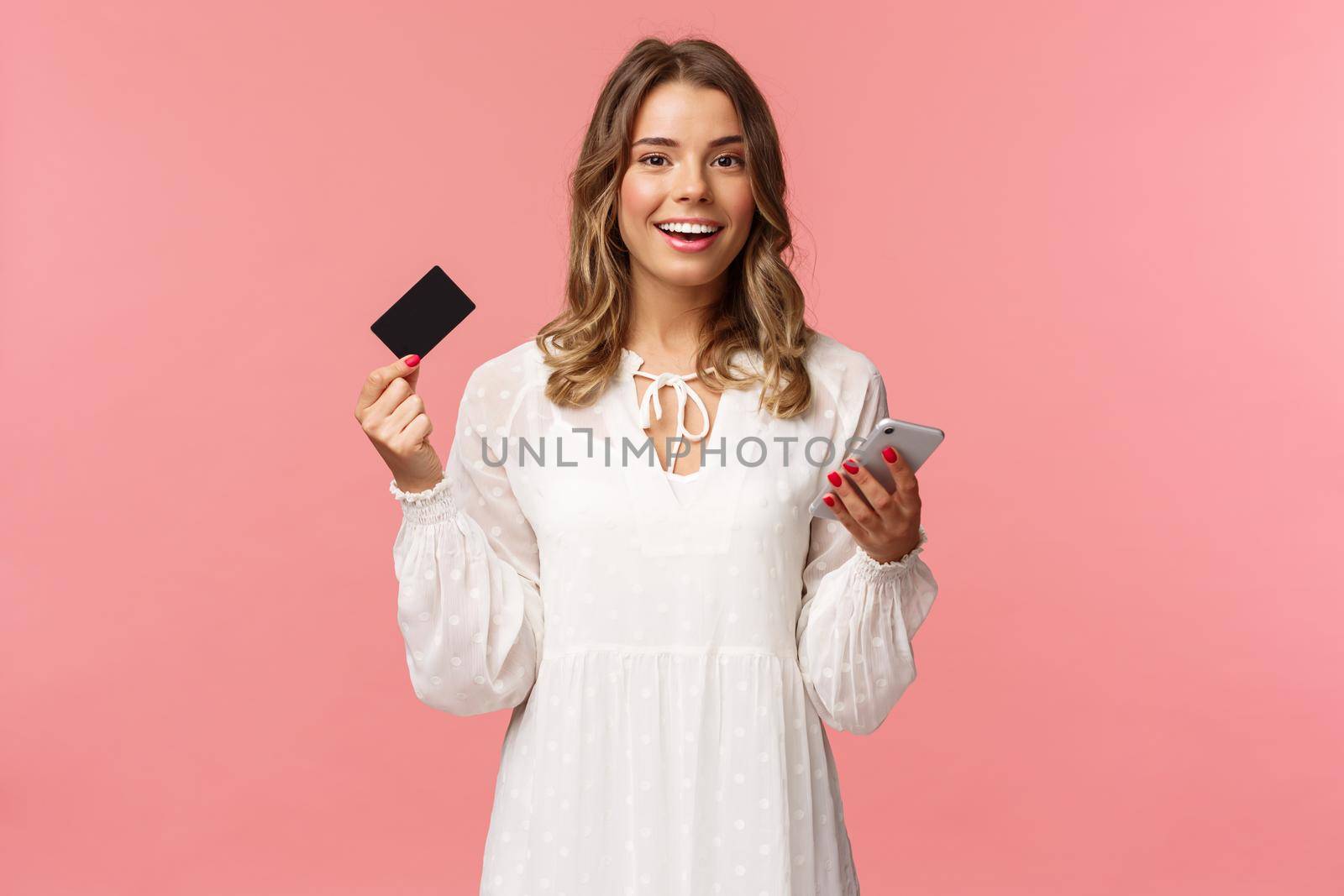 Portrait of carefree young pretty blond woman using mobile phone to pay for online purchase, holding credit card and smiling happy camera, shopping internet, download smartphone app by Benzoix