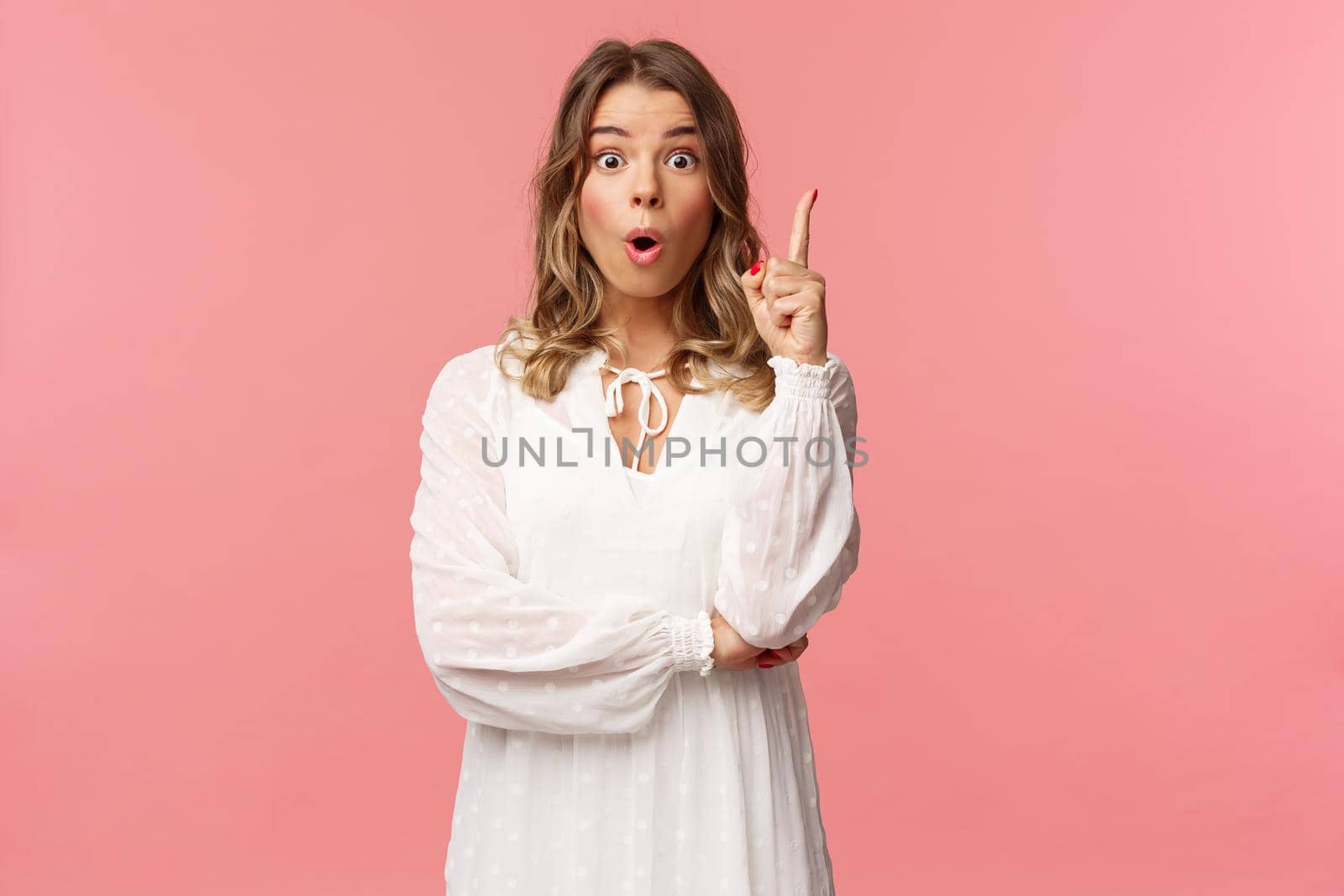 Beauty, fashion and women concept. Portrait of amazed and excited feminine blond girl in white dress, open mouth gasping amused and raise one finger, have suggestion, found solution.