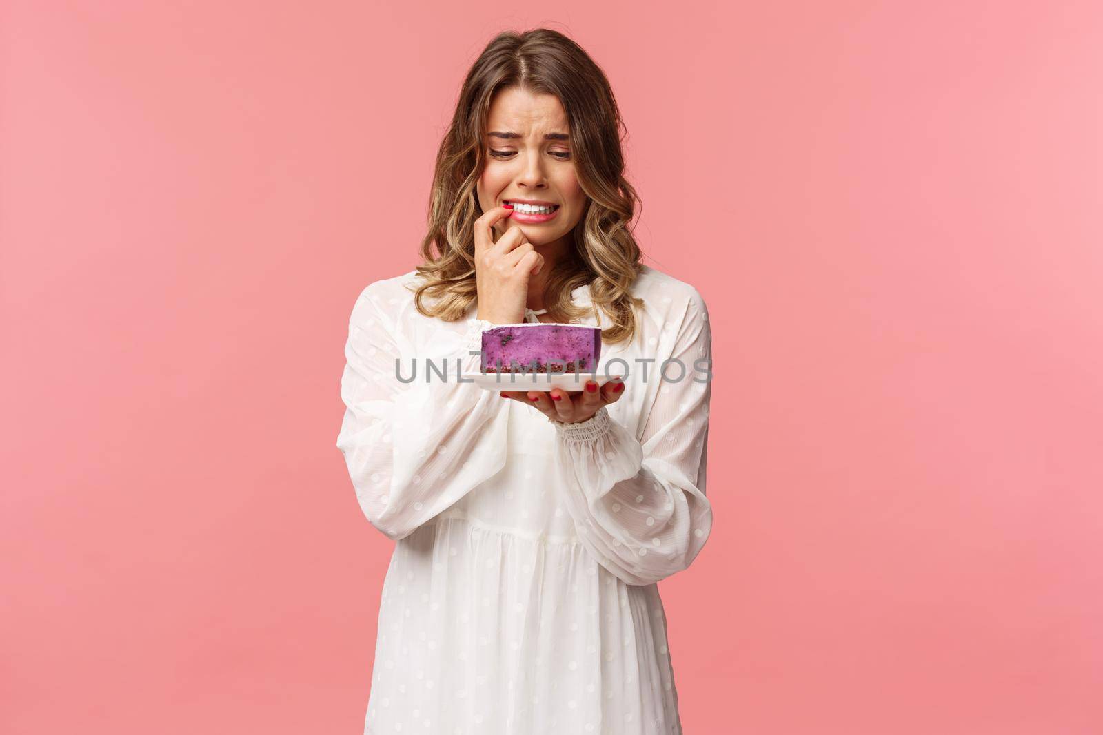 Holidays, spring and party concept. Portrait of nervous blond girl on diet, biting lip cant resist temptation to eat delicious cake, looking at dessert with hesitant expression, grimacing worried.