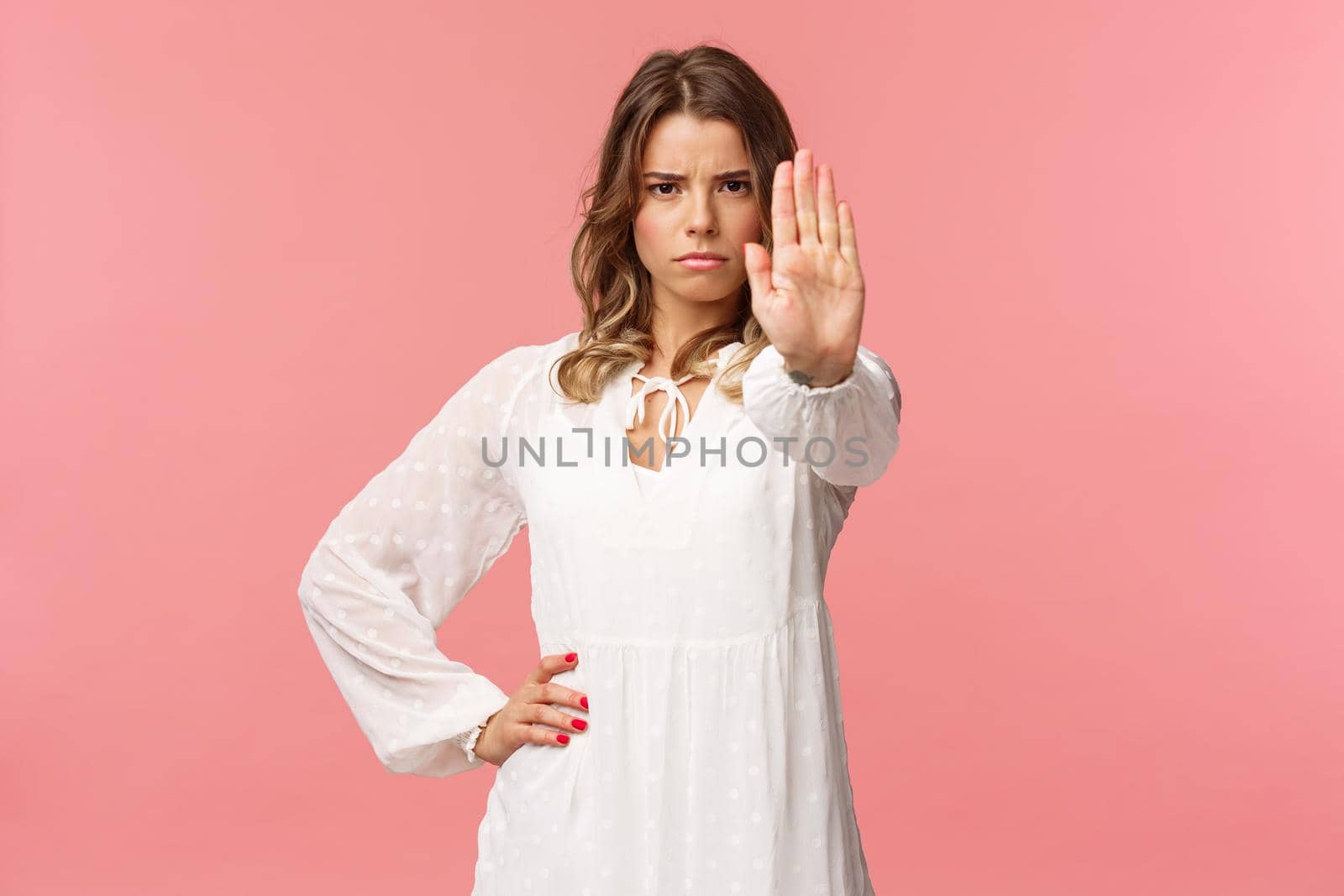 Waist-up portrait of serious-looking assertive and confident young blond female in white dress, extend arm in stop motion, frowning, demand quit, prohibit something, warning express disagreement by Benzoix
