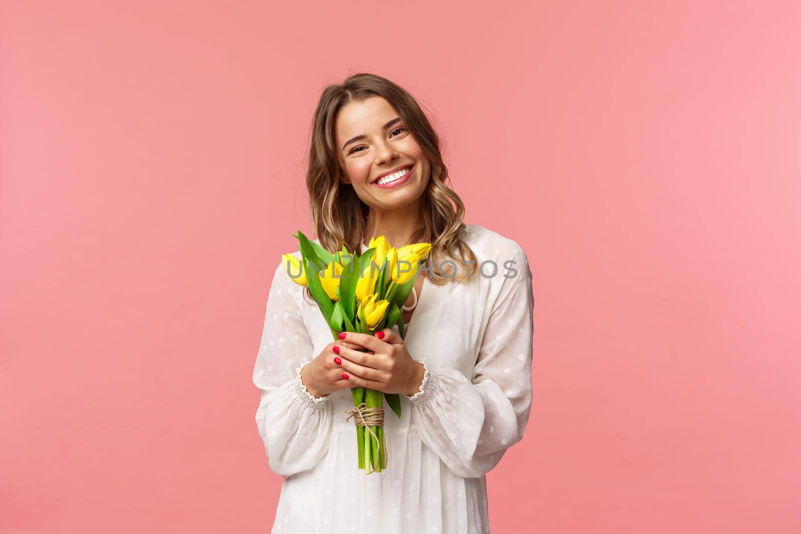 Holidays, beauty and spring concept. Portrait of lovely caucasian blond girl in white dress, smiling upbeat, holding yellow tulips, having perfect romantic date with flowers as gift, pink background by Benzoix