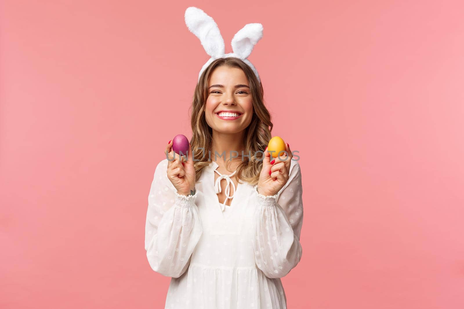 Holidays, spring and party concept. Portrait of lovely, cheerful blond girl in rabbit ears, holding colored eggs, celebrating Easter with family, enjoying spend traditional day with close people by Benzoix