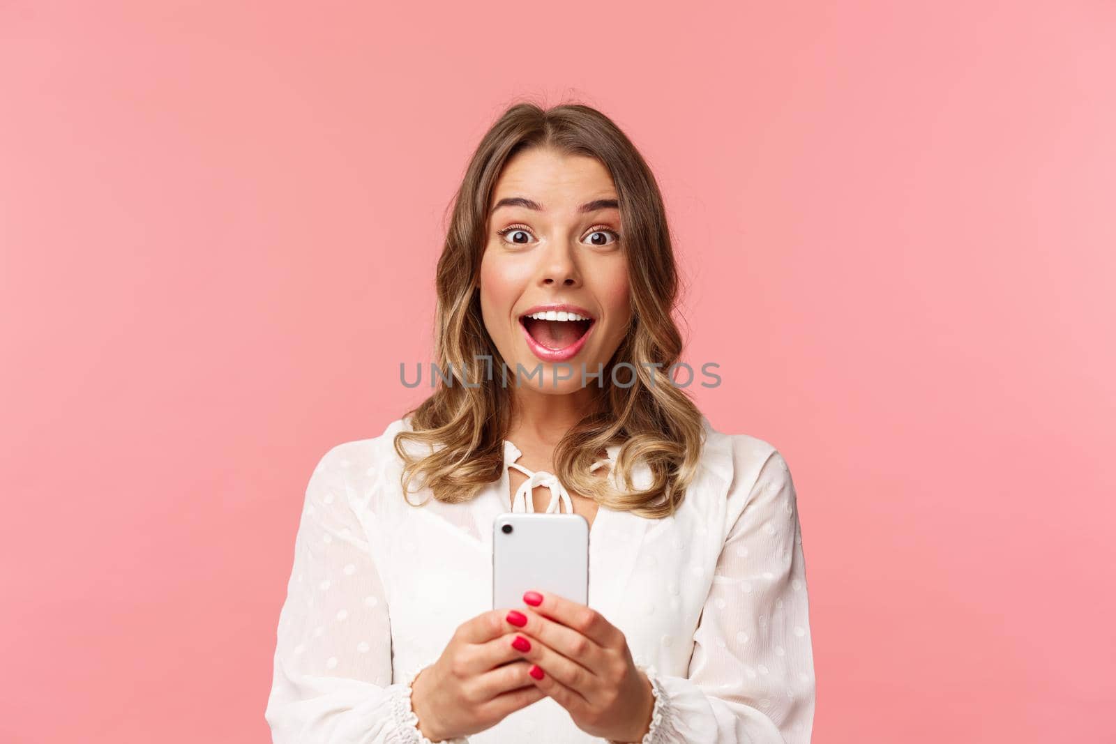 Close-up portrait of excited and amazed young blond girl attend performance of favorite singer, record video, stream online on mobile phone, taking photo with smartphone, look thrilled by Benzoix