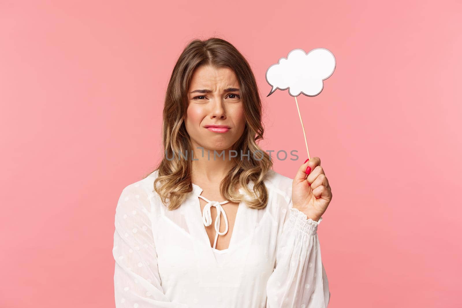 Spring, happiness and celebration concept. Close-up portrait of skeptical and hesitant young blond girl express dislike or reluctance, holding commend cloud stick near head, grimacing disappointed.