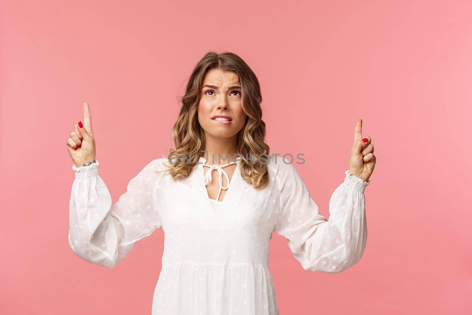 Skeptical and embarrassed blond caucasian woman in white cute dress, grimacing, cringe from seeing something disgusting, frowning doubtful and pointing fingers up strange thing, pink background by Benzoix