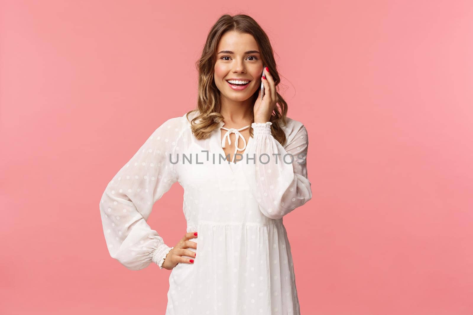 Portrait of joyful good-looking blond woman in white dress, talking on phone, hold smartphone near ear and look upbeat camera, smiling discuss friends date, stand pink background by Benzoix