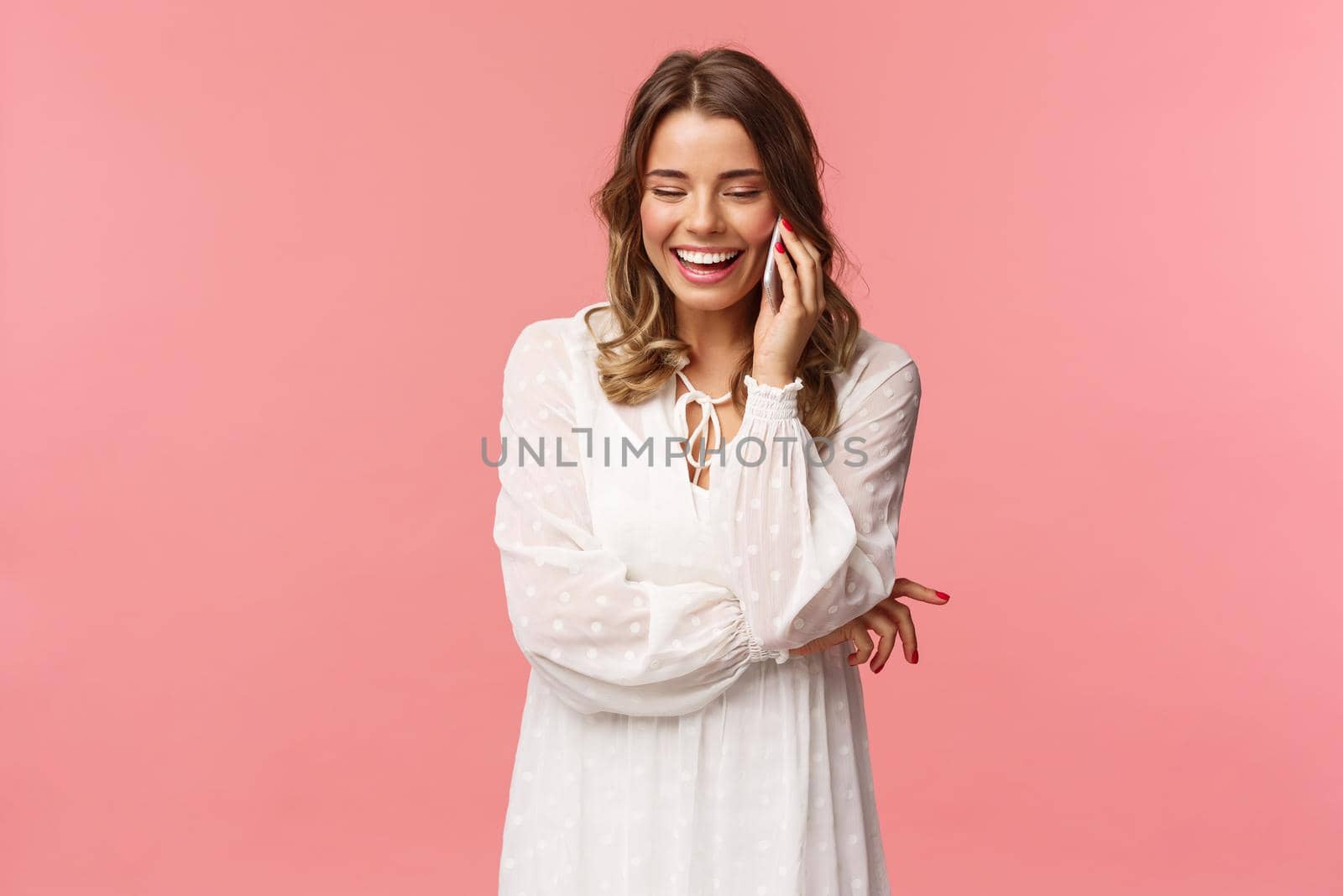 Communication and technology concept. Attractive caucasian female in white dress, blond short haircut, hold smartphone, talking on mobile phone and laughing, smiling carefree, pink background by Benzoix