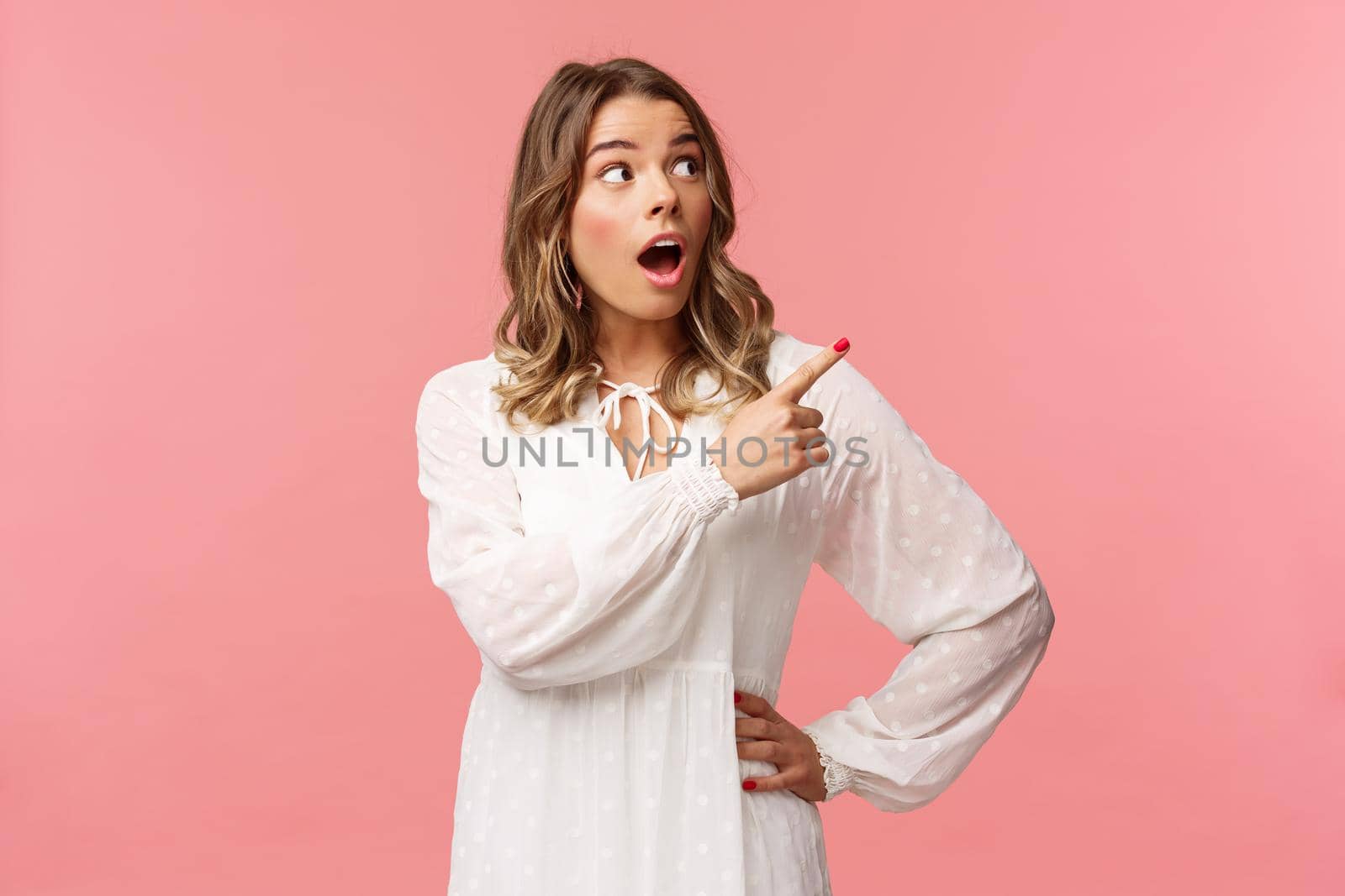 Surprised and excited good-looking blond girl in white cute dress, open mouth in amazement, look curious pointing upper right corner astonished, see something awesome, pink background by Benzoix