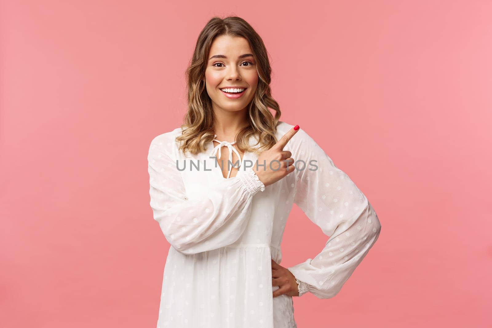 Upbeat good-looking caucasian blond girl in white dress, pointing upper right corner and smiling at camera with interested, curious face discuss special promo spring discounts, pink background by Benzoix