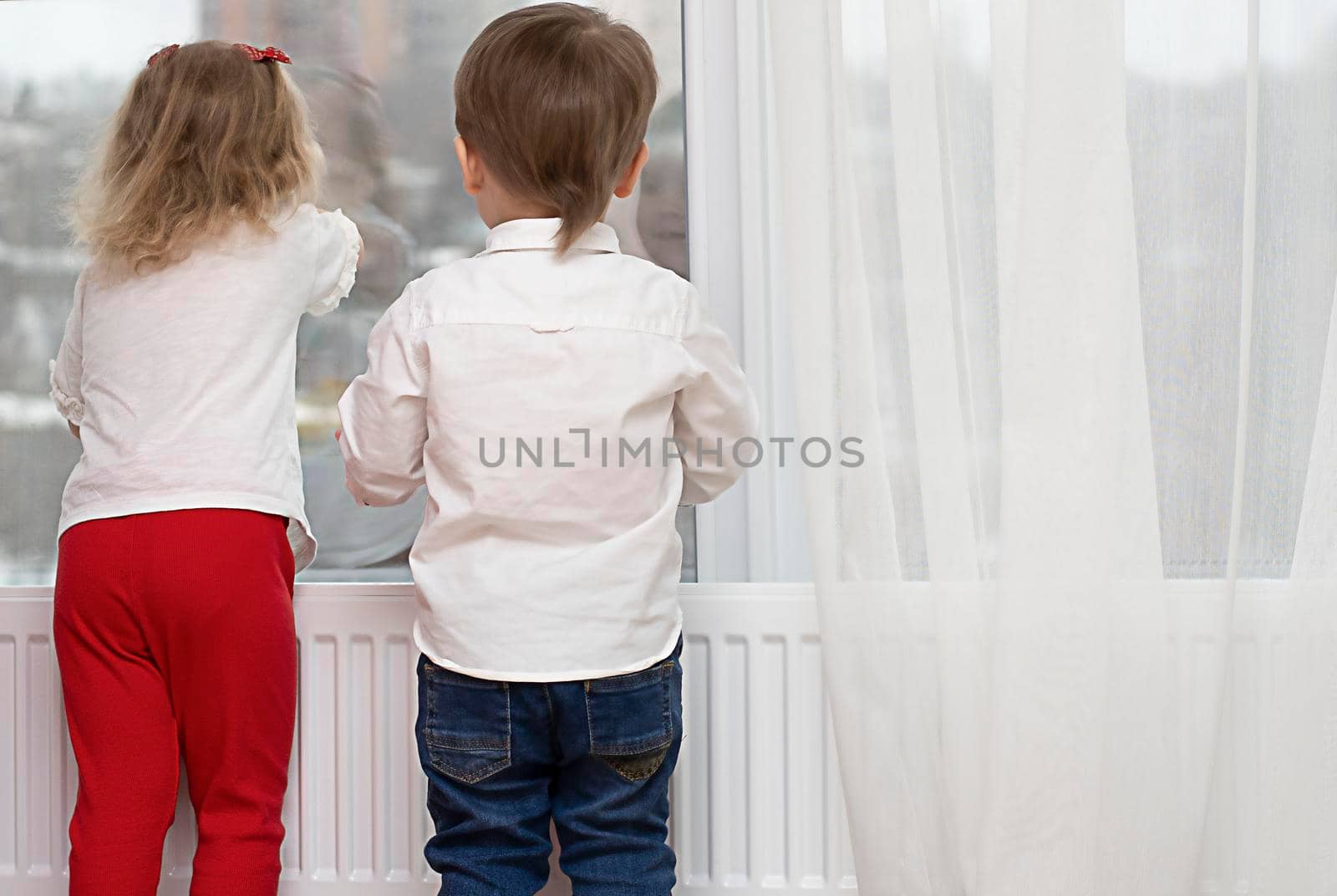 Little boy and girl are standing near the window. Expectation, hope, dream. copy space, peace.