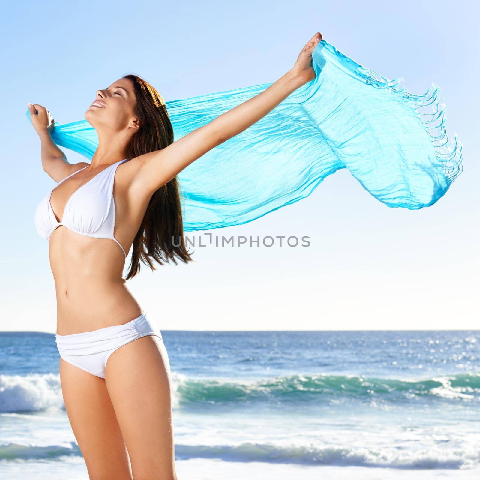 A beautiful young woman holding a sarong thats blowing in the wind.