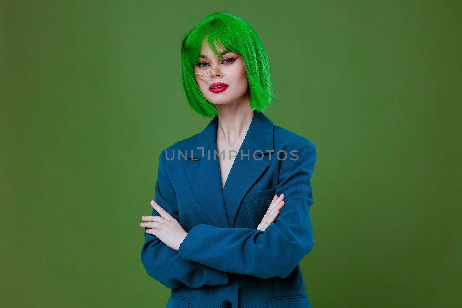 Portrait of a charming lady wearing a green wig blue jacket posing green background unaltered. High quality photo