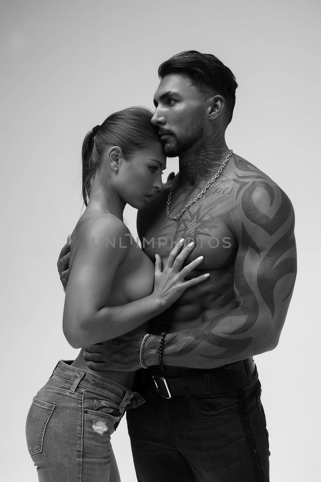 Black and white tattooed shirtless man and seductive topless woman looking away