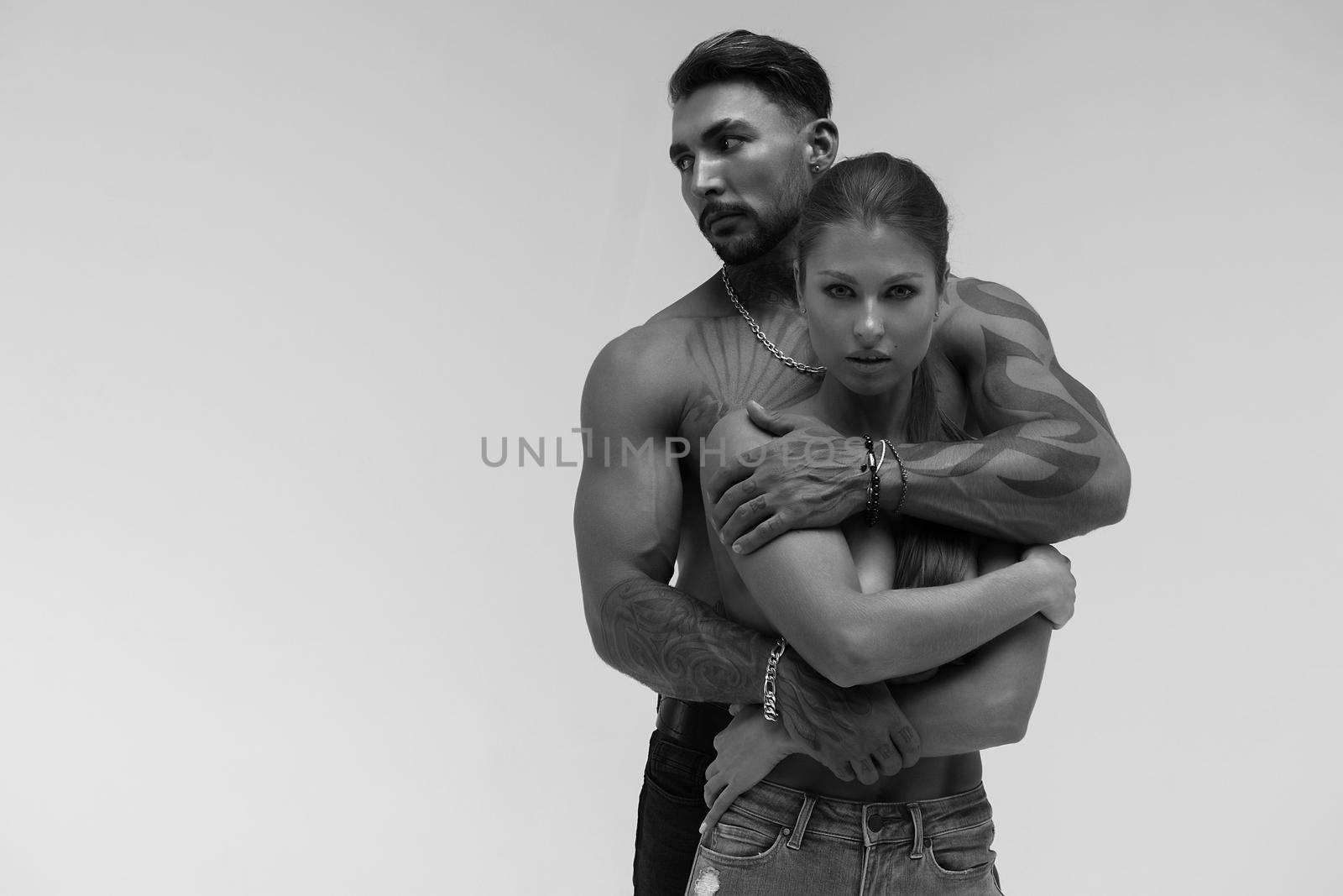 Black and white tattooed shirtless man and seductive topless woman looking away