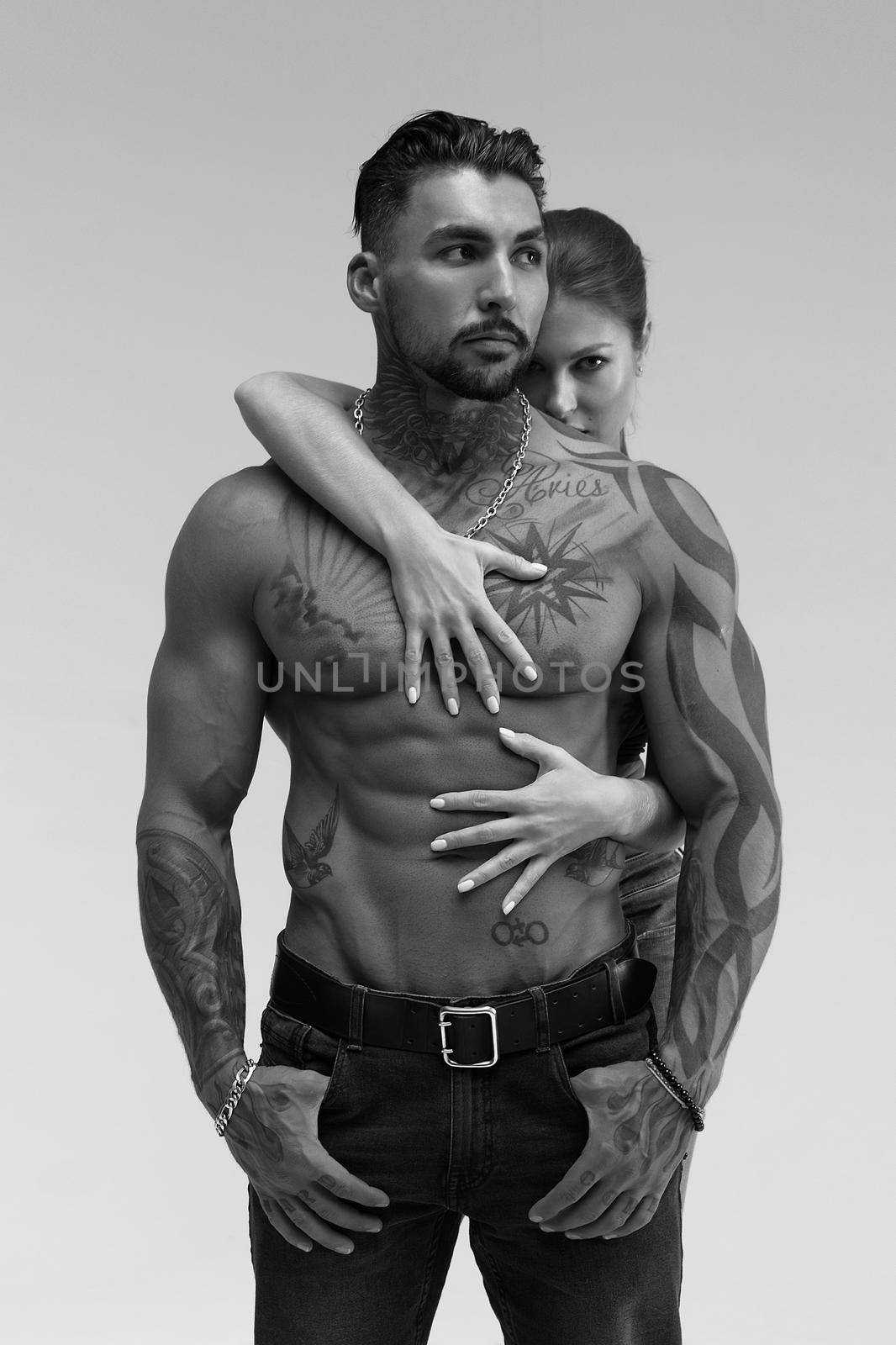 Black and white side view of topless woman and shirtless man looking at camera against gray background