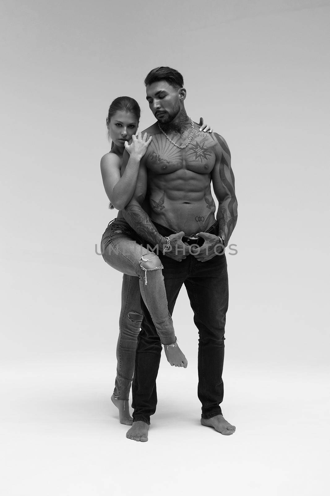 Black and white side view of topless woman and shirtless man looking at camera against gray background