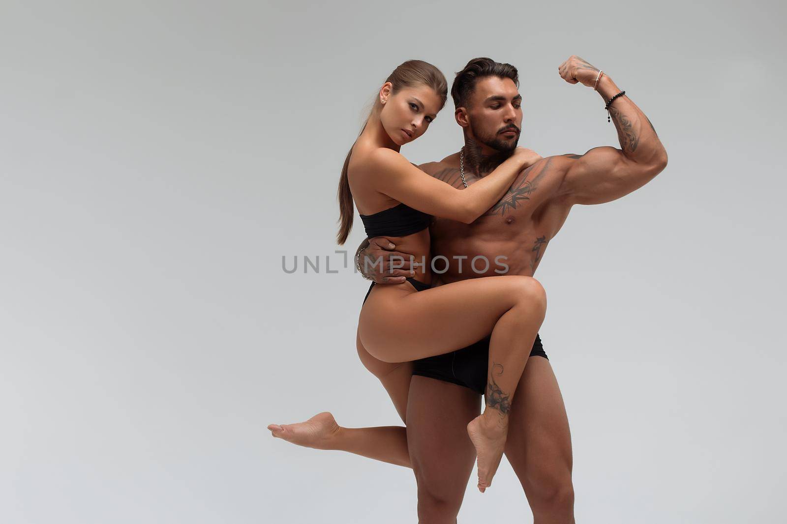 Muscular tattooed man embracing slim topless woman in panties on gray background