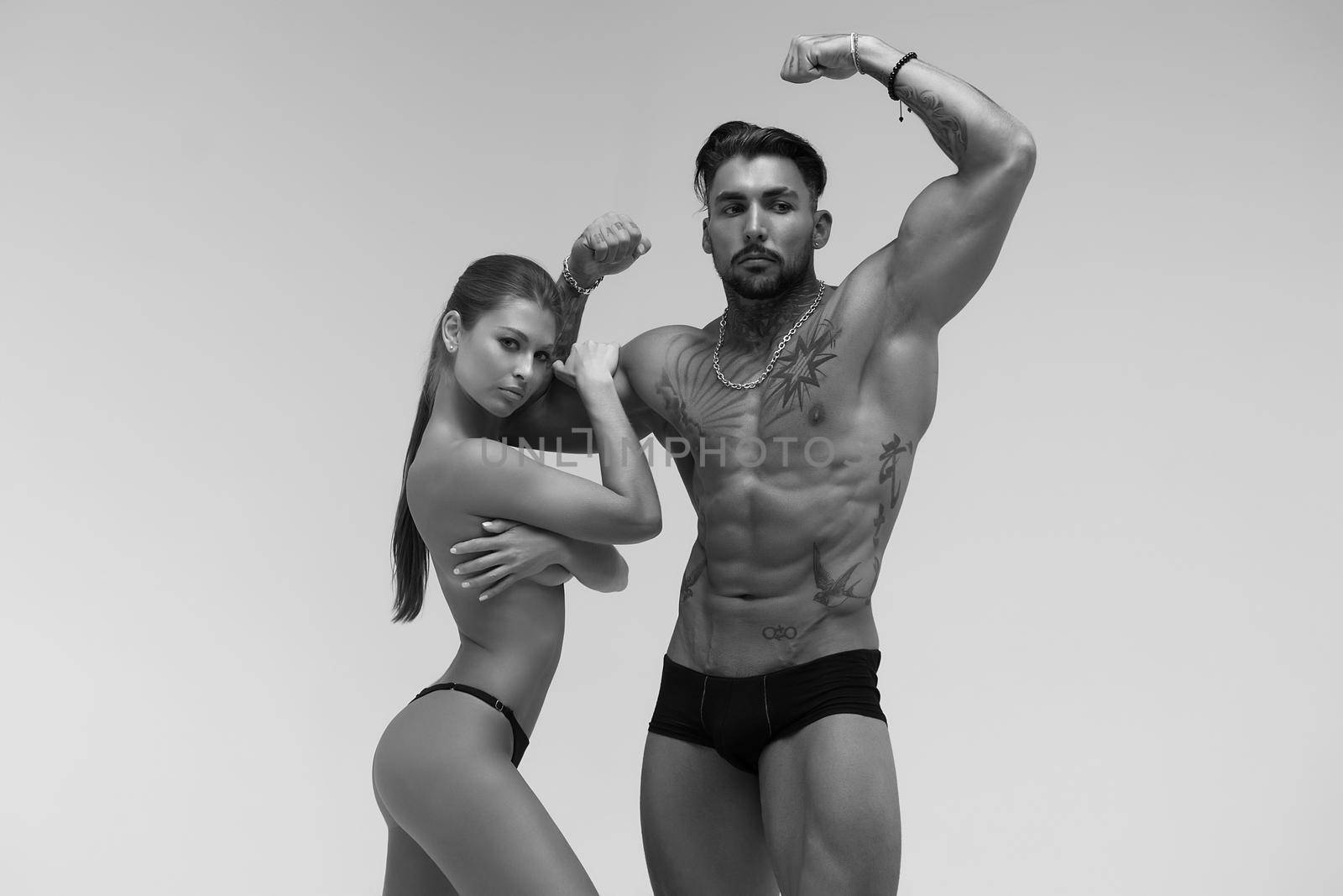 Black and white tattooed shirtless man and seductive topless woman looking away