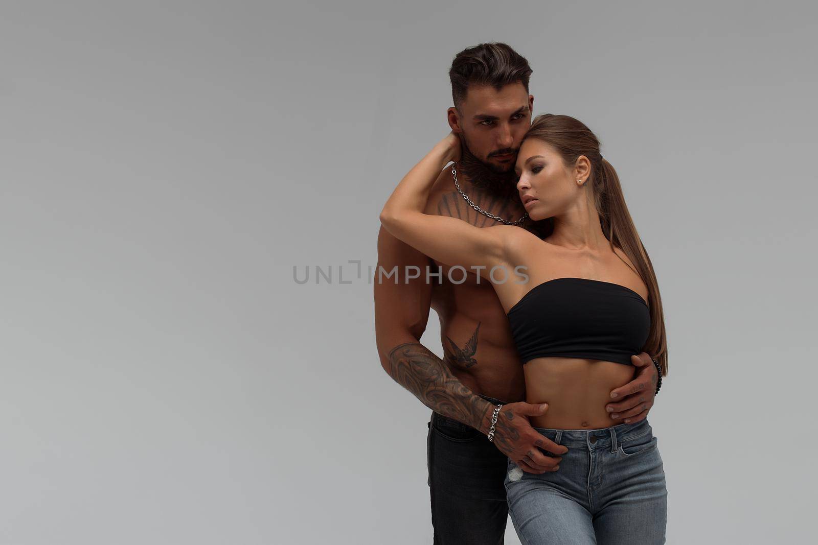 Muscular tattooed man embracing slim topless woman in panties on gray background