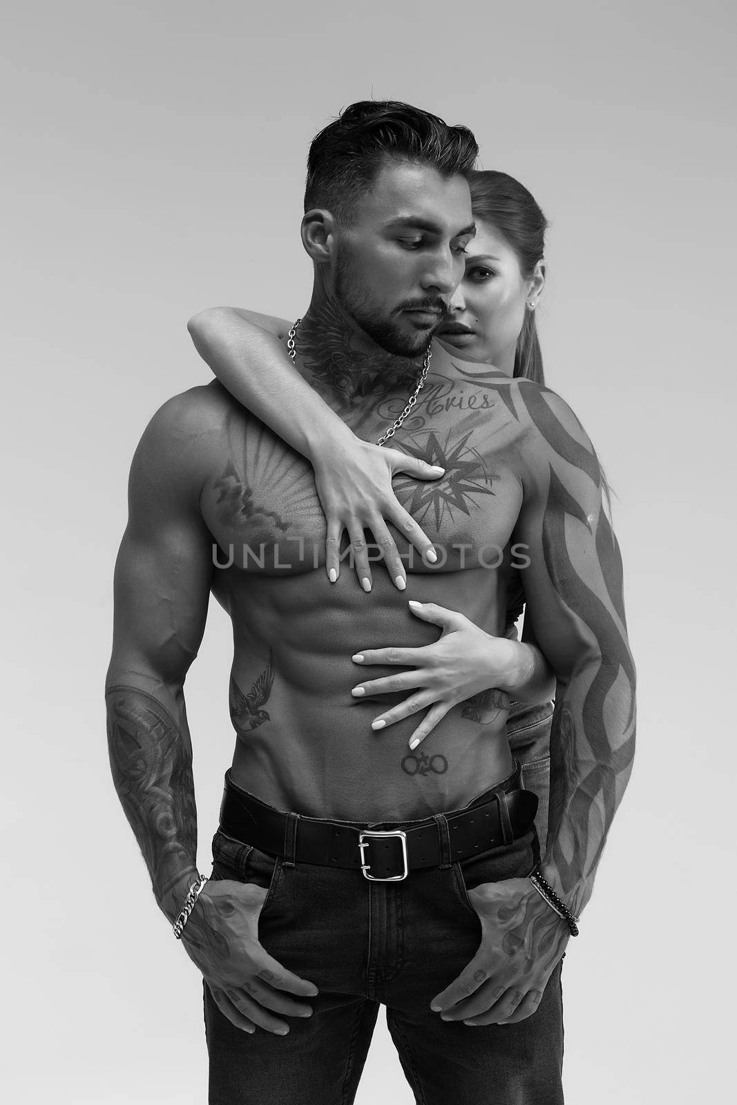 Black and white side view of topless woman and shirtless man looking at camera against gray background