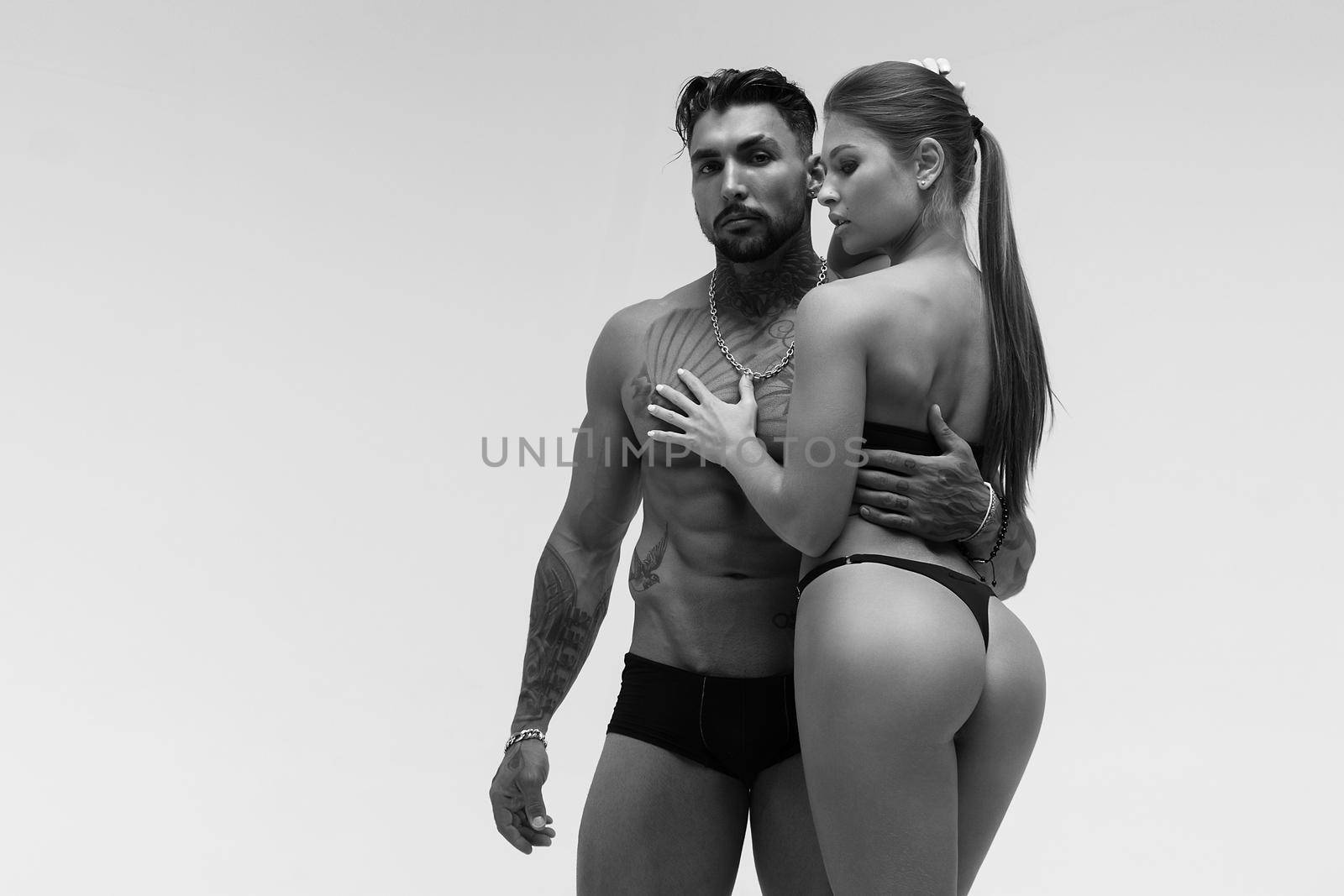 Black and white tattooed shirtless man and seductive topless woman looking away