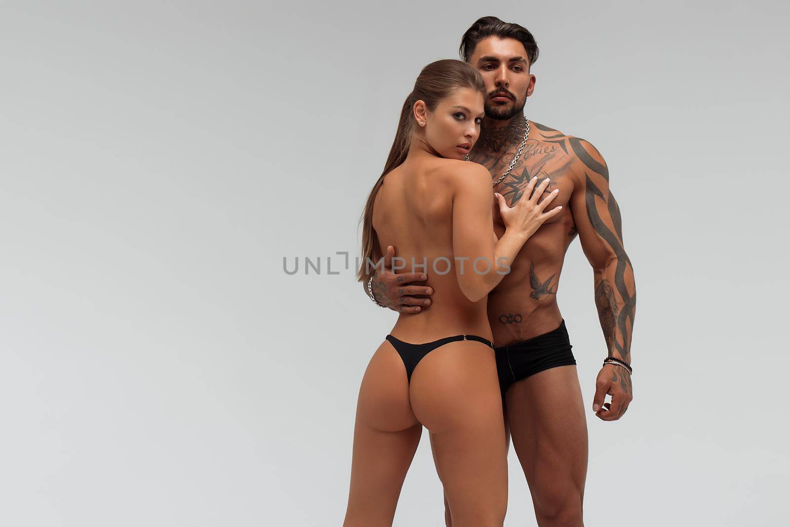 Muscular tattooed man embracing slim topless woman in panties on gray background