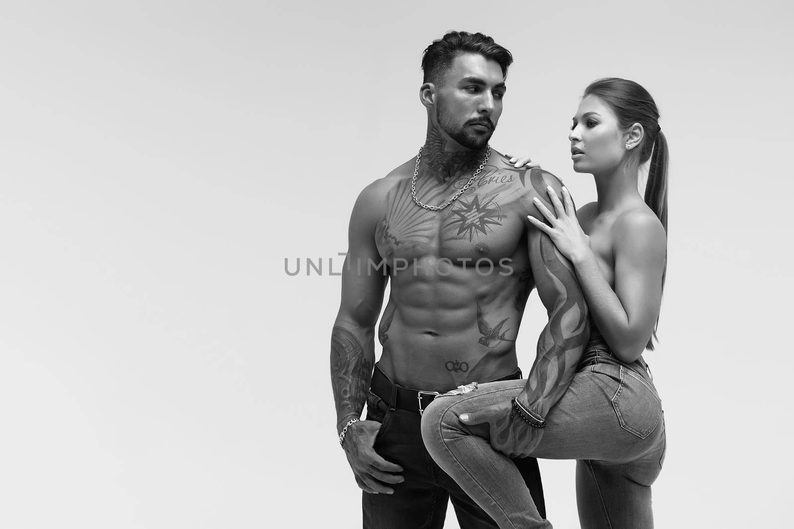 Black and white tattooed shirtless man and seductive topless woman looking away