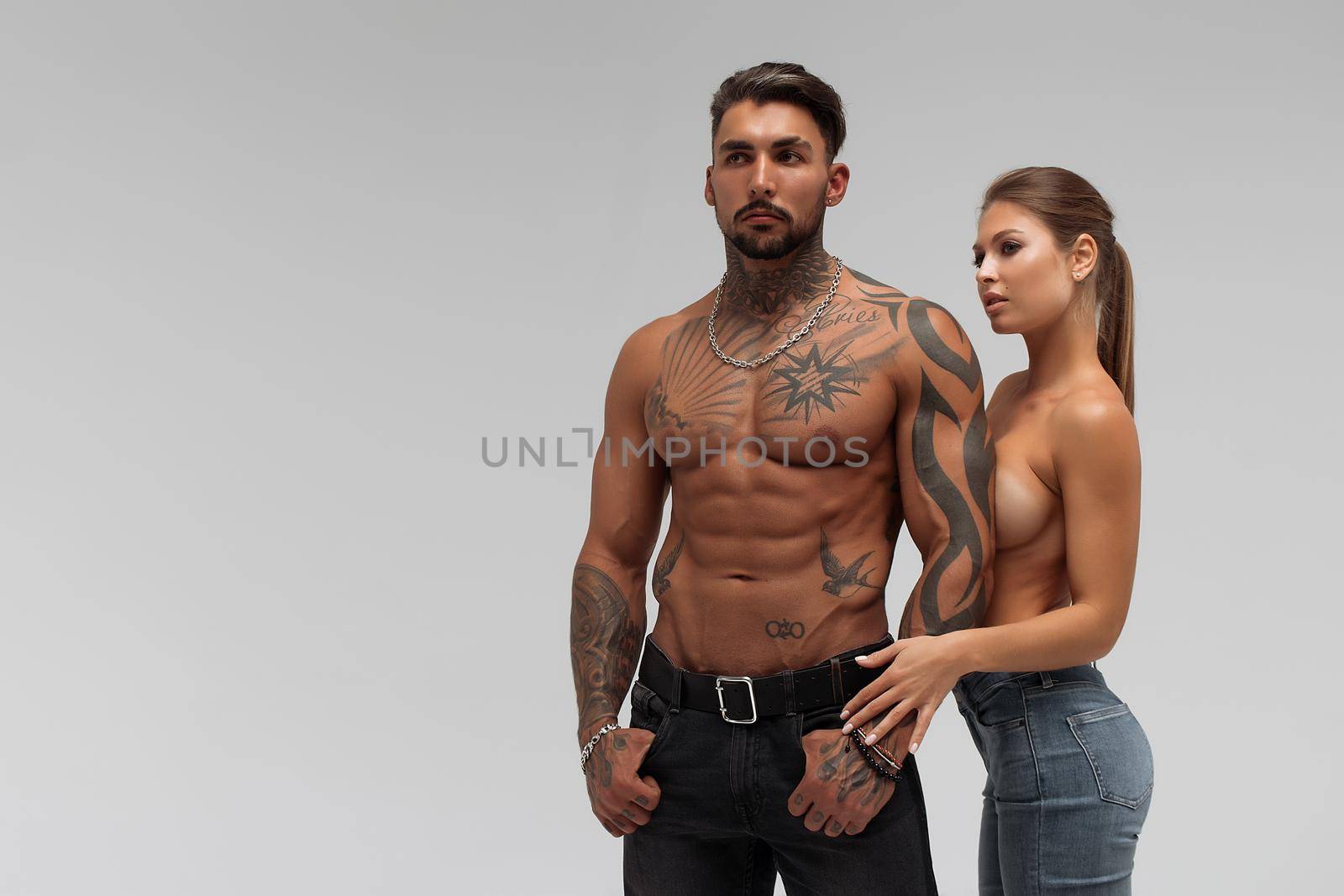 Muscular tattooed man embracing slim topless woman in panties on gray background