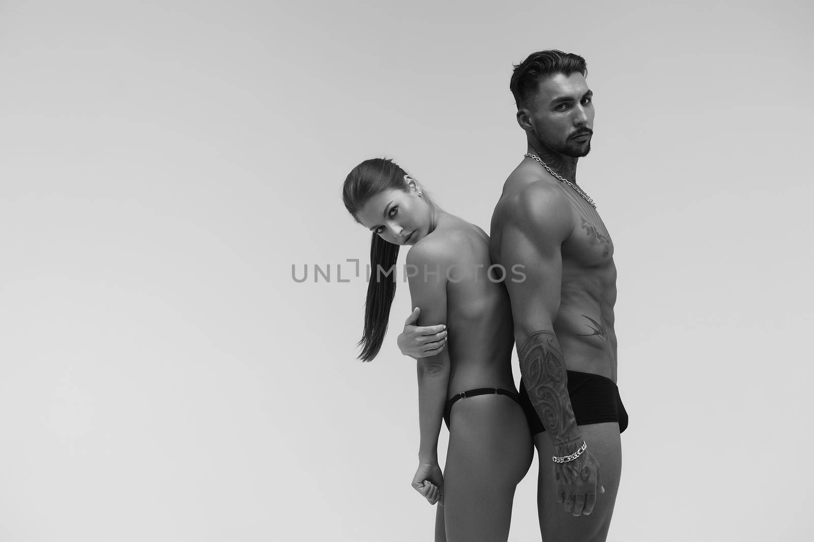 Black and white tattooed shirtless man and seductive topless woman looking away