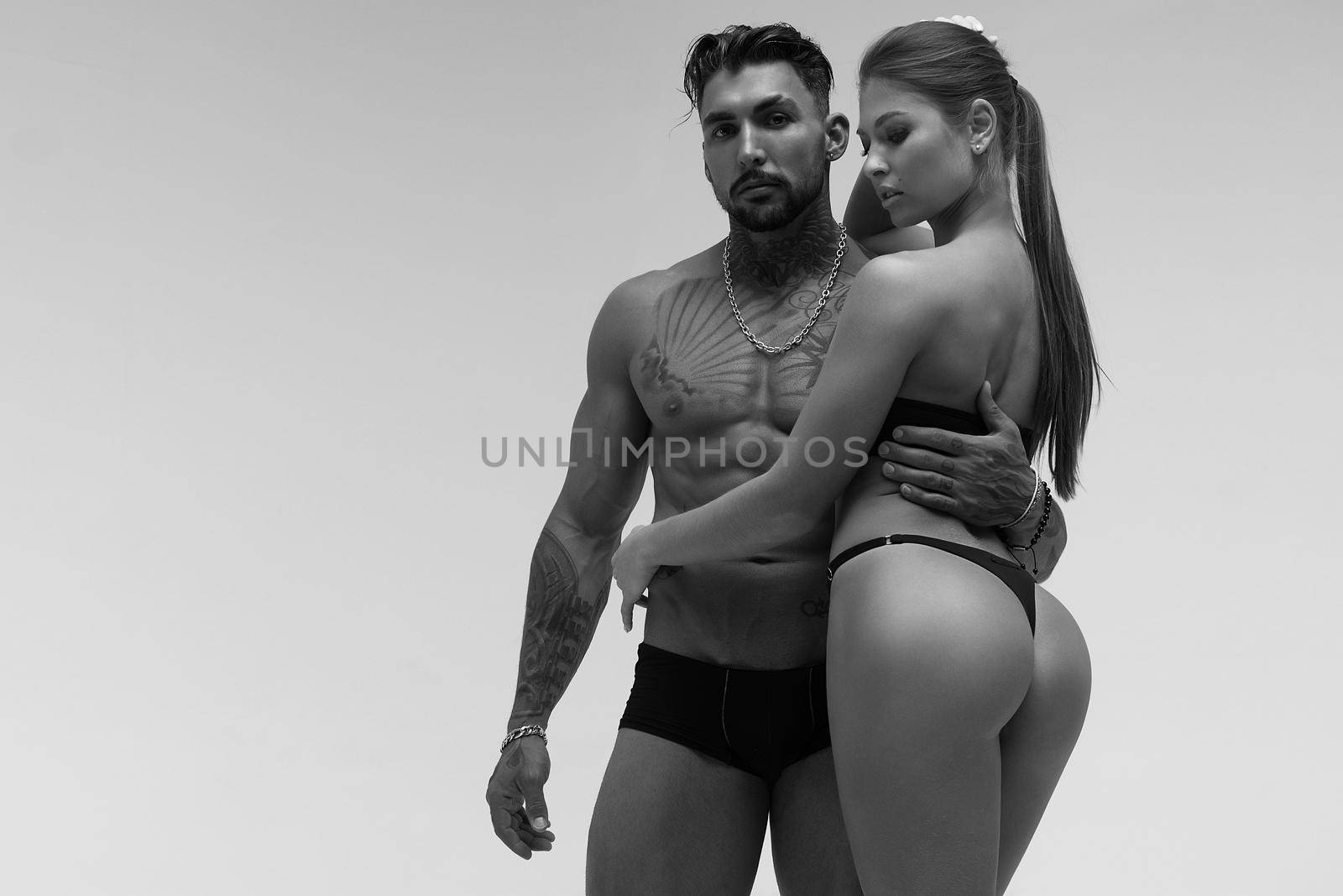 Black and white tattooed shirtless man and seductive topless woman looking away